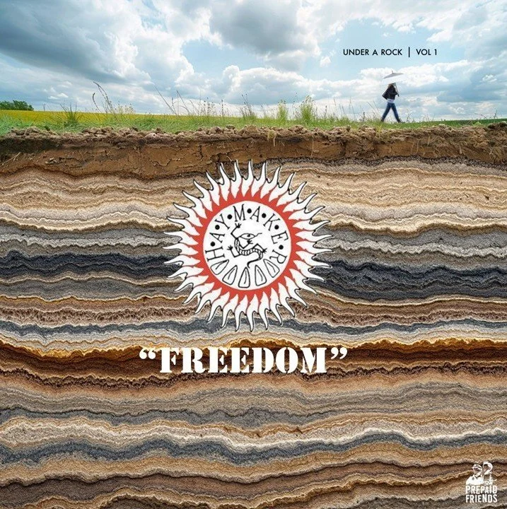 Cross-section of layered rock with a person walking on the ground surface holding an umbrella in a green landscape under a cloudy sky. Added graphic of a circular emblem with a bird and the words 'HAY MAKE' and the title 'UNDER A ROCK VOL 1' at the top, and the word 'FREEDOM' below the emblem.