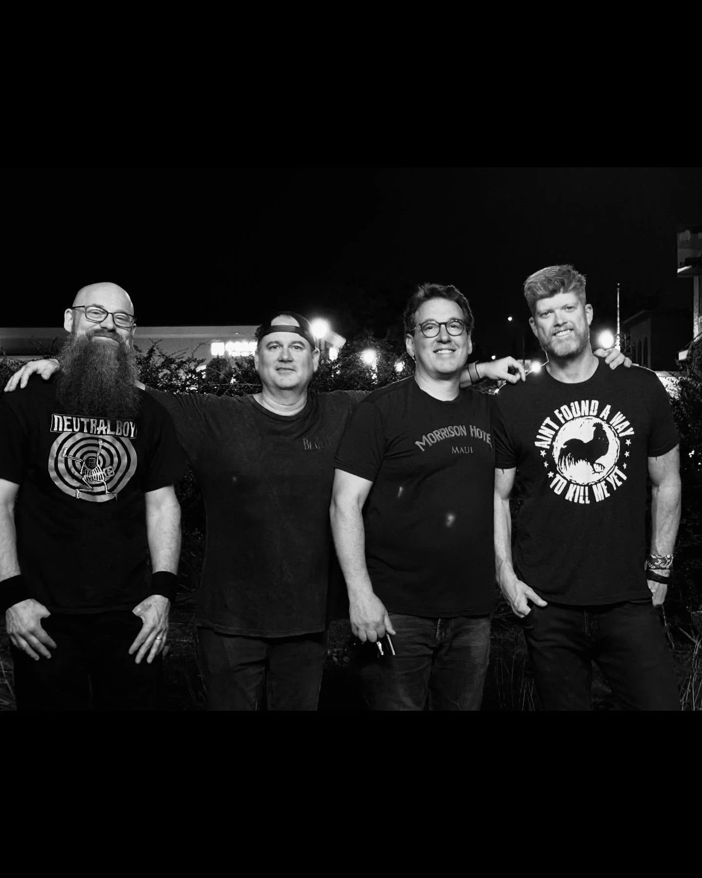 Group of five men standing outdoors at night, smiling, with their arms around each other, in a casual setting.