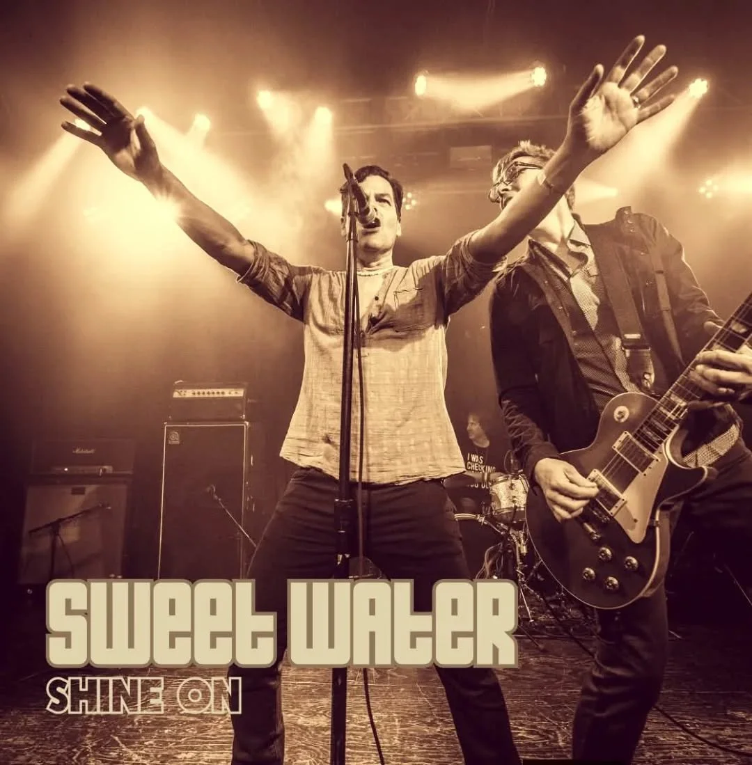 Two male musicians performing on stage, one singing into a microphone with arms outstretched, the other playing an electric guitar. The scene is illuminated with bright stage lights in the background. The image has a sepia tone with the band name 'Sweet Water' and the album title 'Shine On' displayed at the bottom.