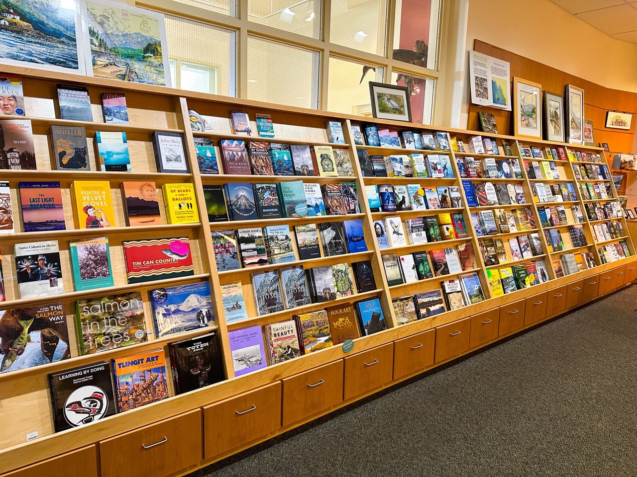 Bookshelves filled with various books in a bookstore with artwork and framed pictures on the walls.