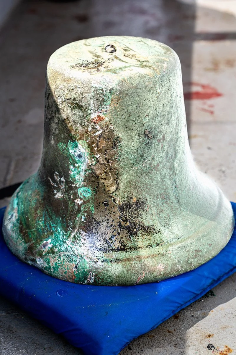A close-up of a weathered, greenish, corroded object with an irregular surface, placed on a blue padded surface on a concrete floor.