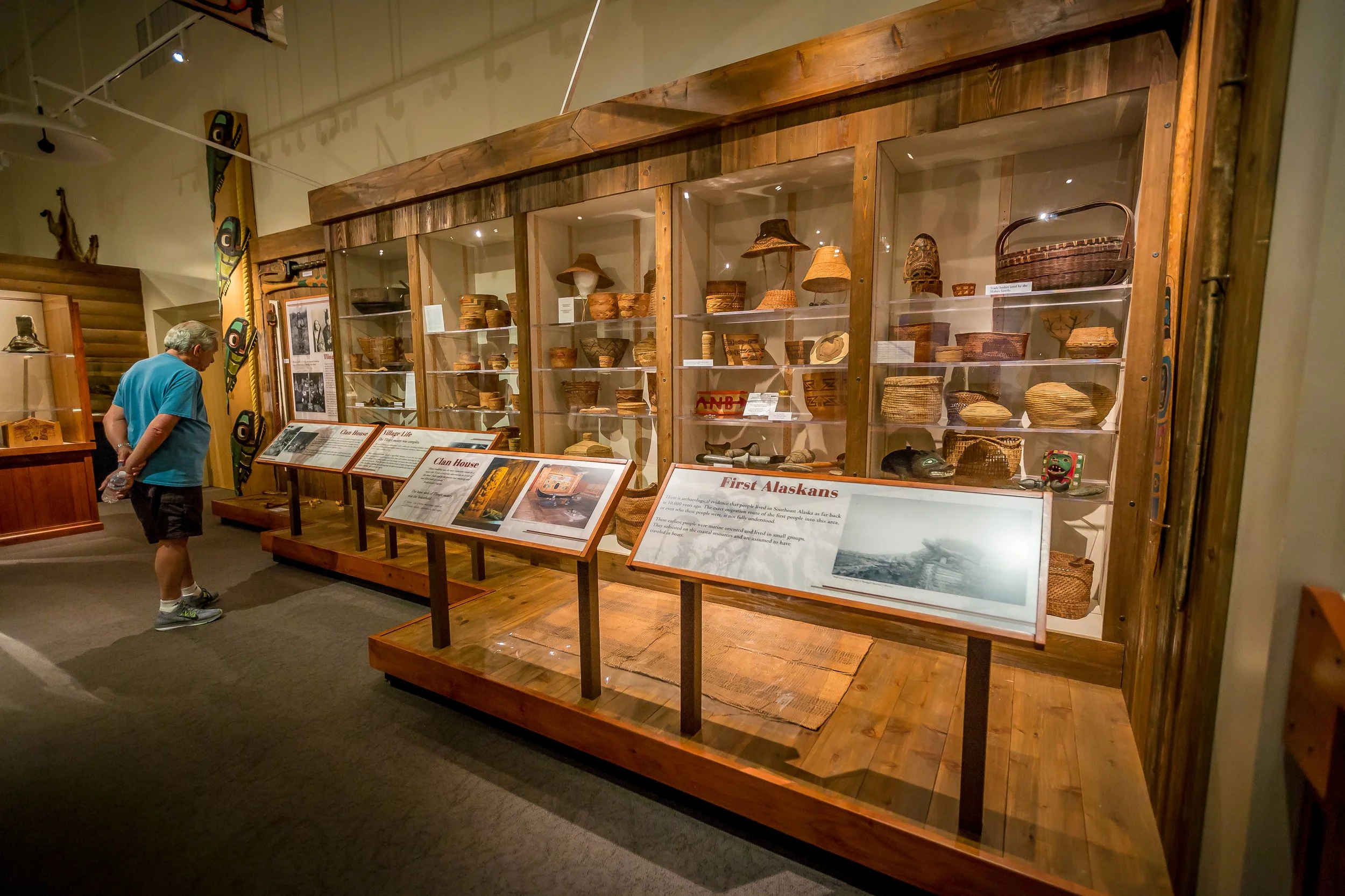 Visitor observing native baskets and artifacts displayed in a museum exhibit case with informational plaques.