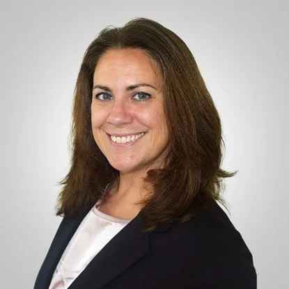 A professional woman with shoulder-length brown hair, wearing a dark blazer and white top, smiling against a plain white background.