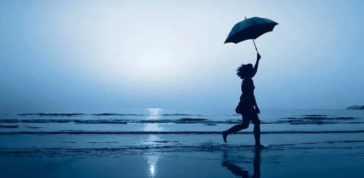 Person holding an umbrella and running along the beach at sunset or sunrise.