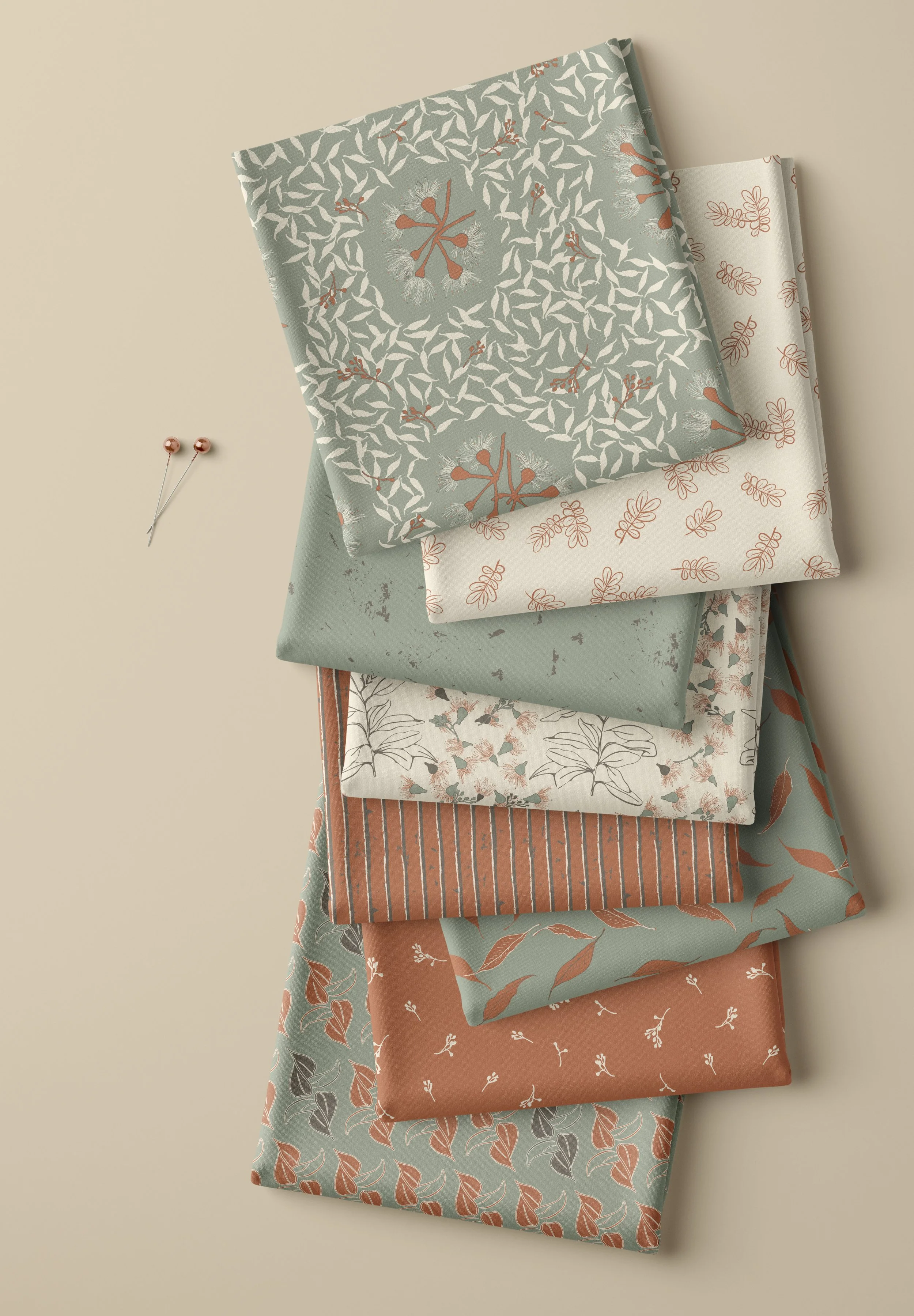 Folded fabrics from the Beneath the Gums collection in soft eucalyptus green, earthy rust and cream botanical patterns.