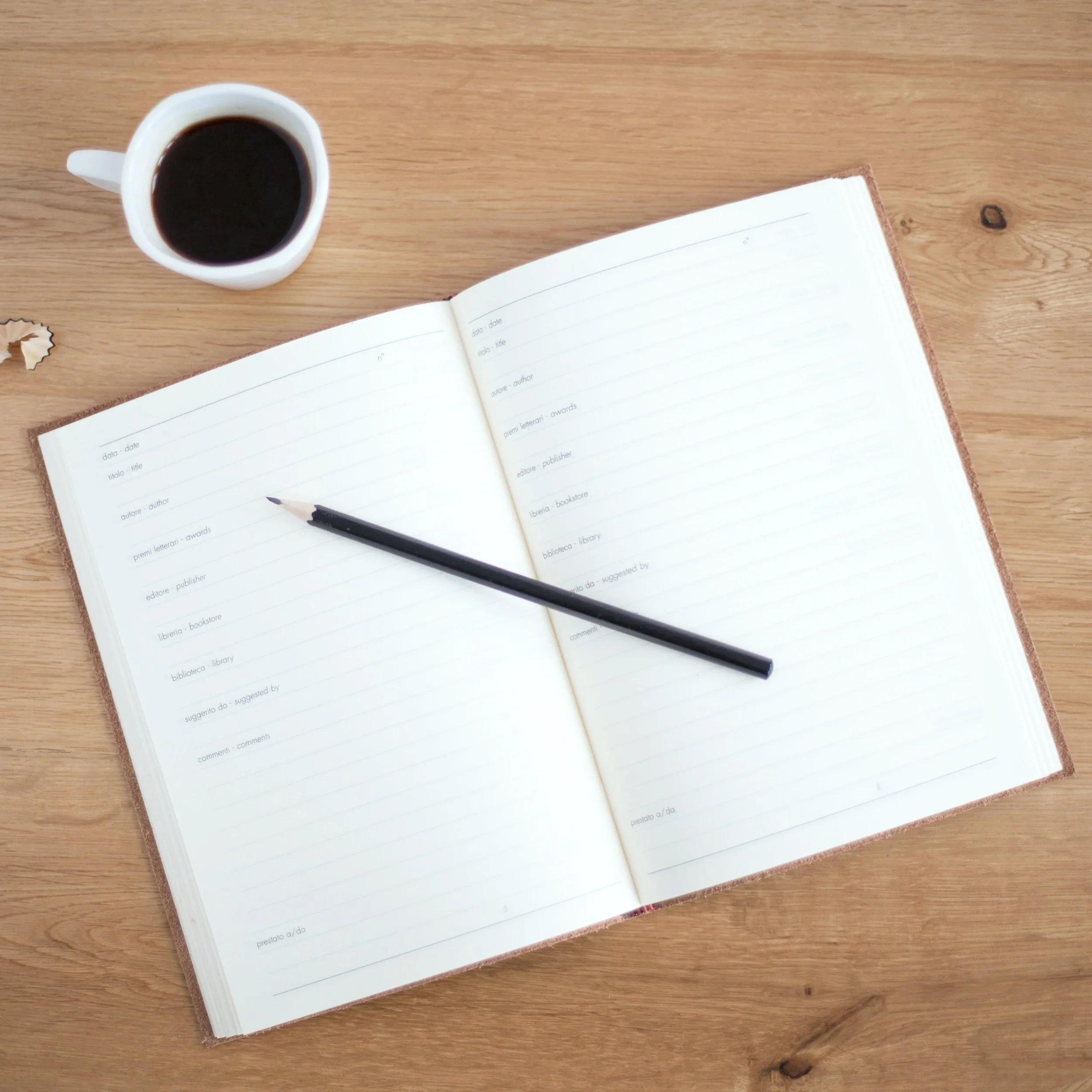 Une tasse de café noir, un carnet ouvert avec une liste, et un stylo noir sur une surface en bois.