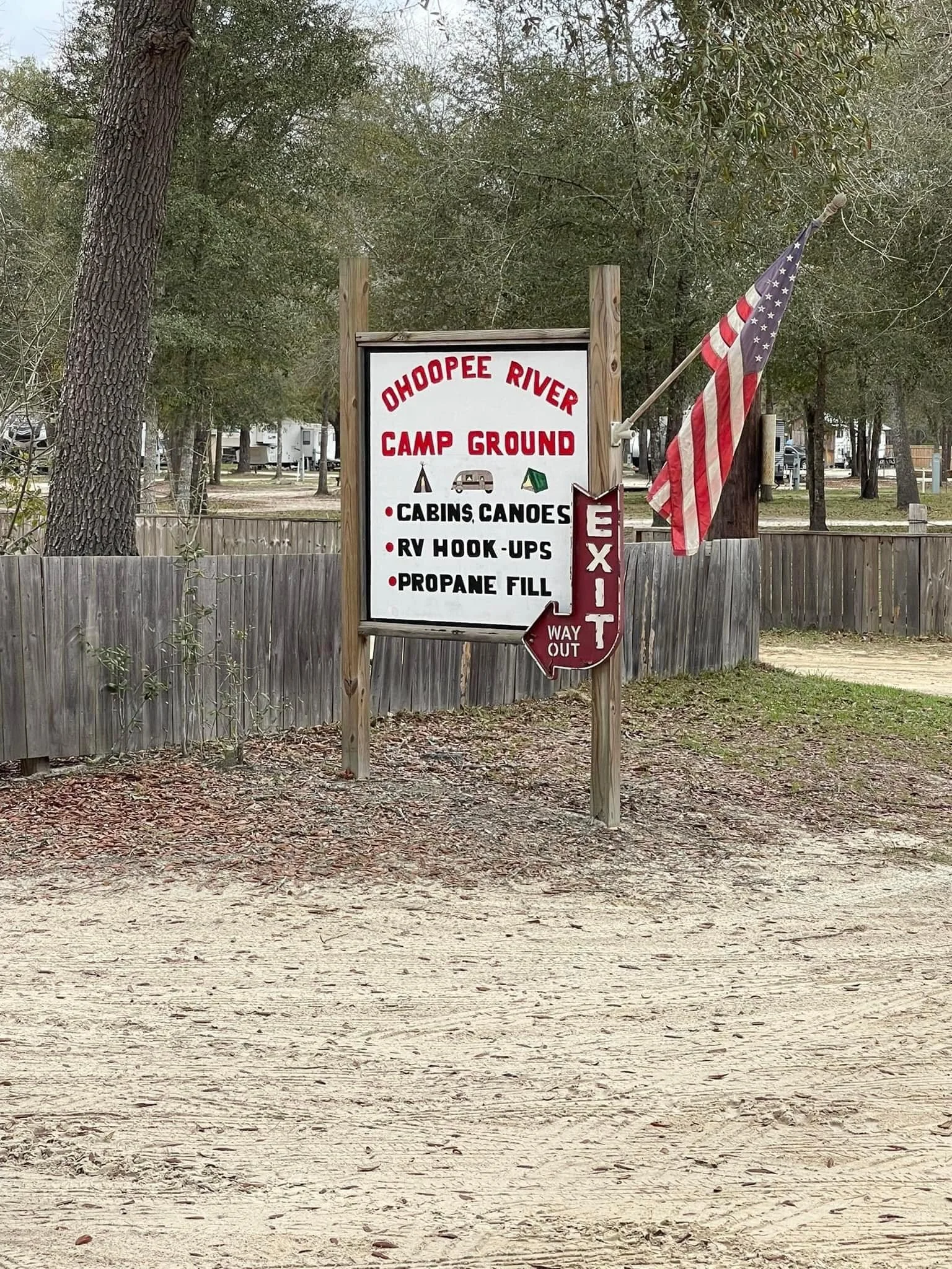 Sign at Ohoopee River Campground listing amenities like cabins, canoes, RV hook-ups, and propane fill, with American flag and exit sign.