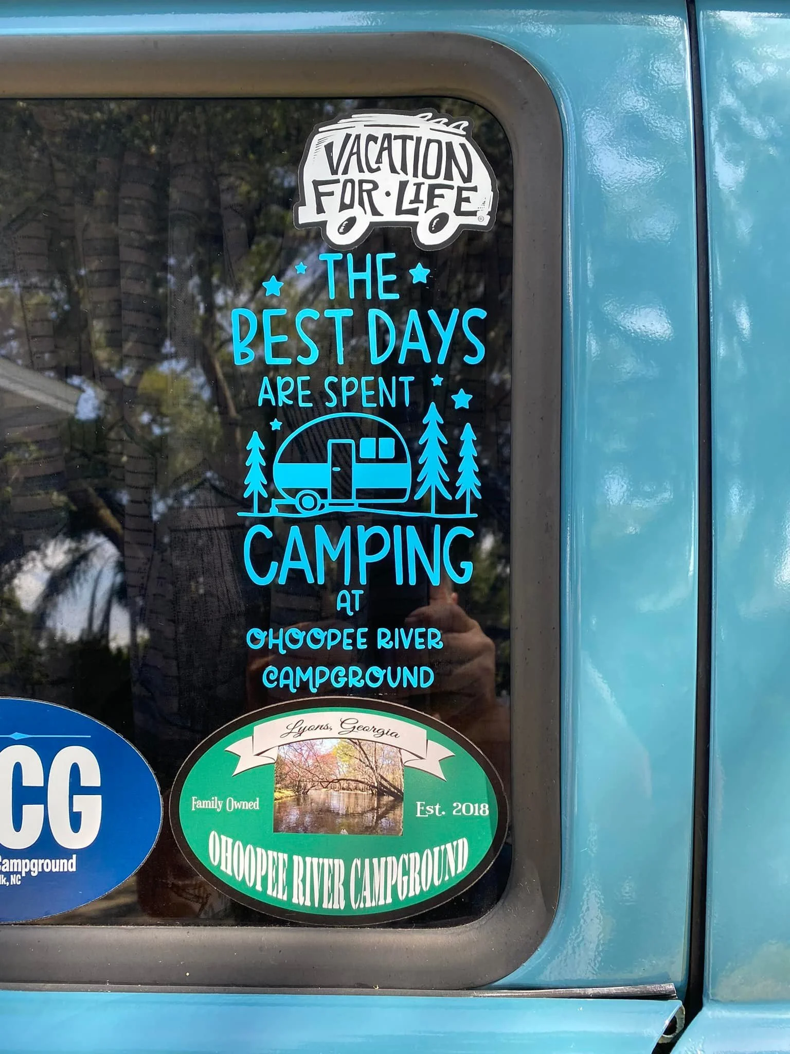 Sticker on a blue vehicle window promoting camping at the Choopee River Campground, with the phrase "The best days are spent camping" and an illustration of a camper surrounded by trees.