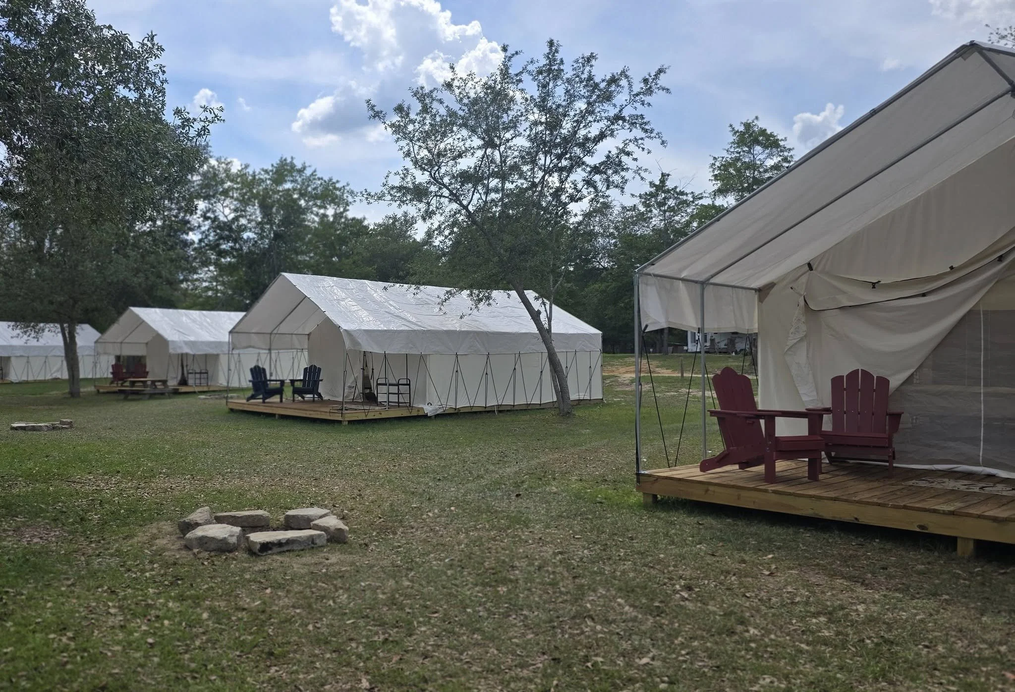 White glamping tents with a fire pit and Adirondack chairs at Ohoopee River RV & Camp Resort