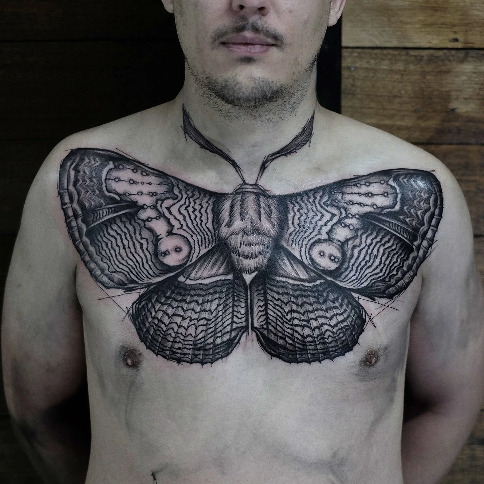 Large detailed blackwork tattoo of a moth covering his chest, extending across his shoulders by Jak