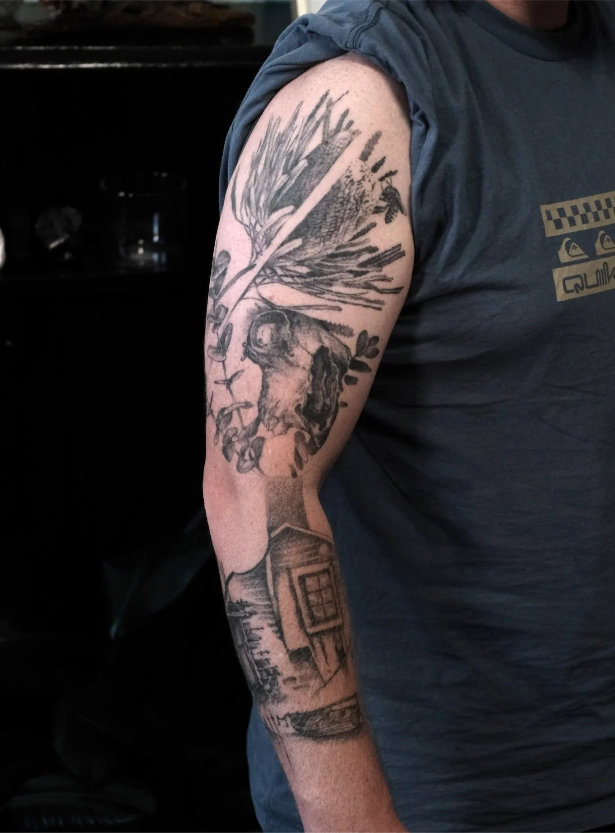 Black and gray tattoo sleeve on person's upper arm with skull and banksia tattooed by Jak