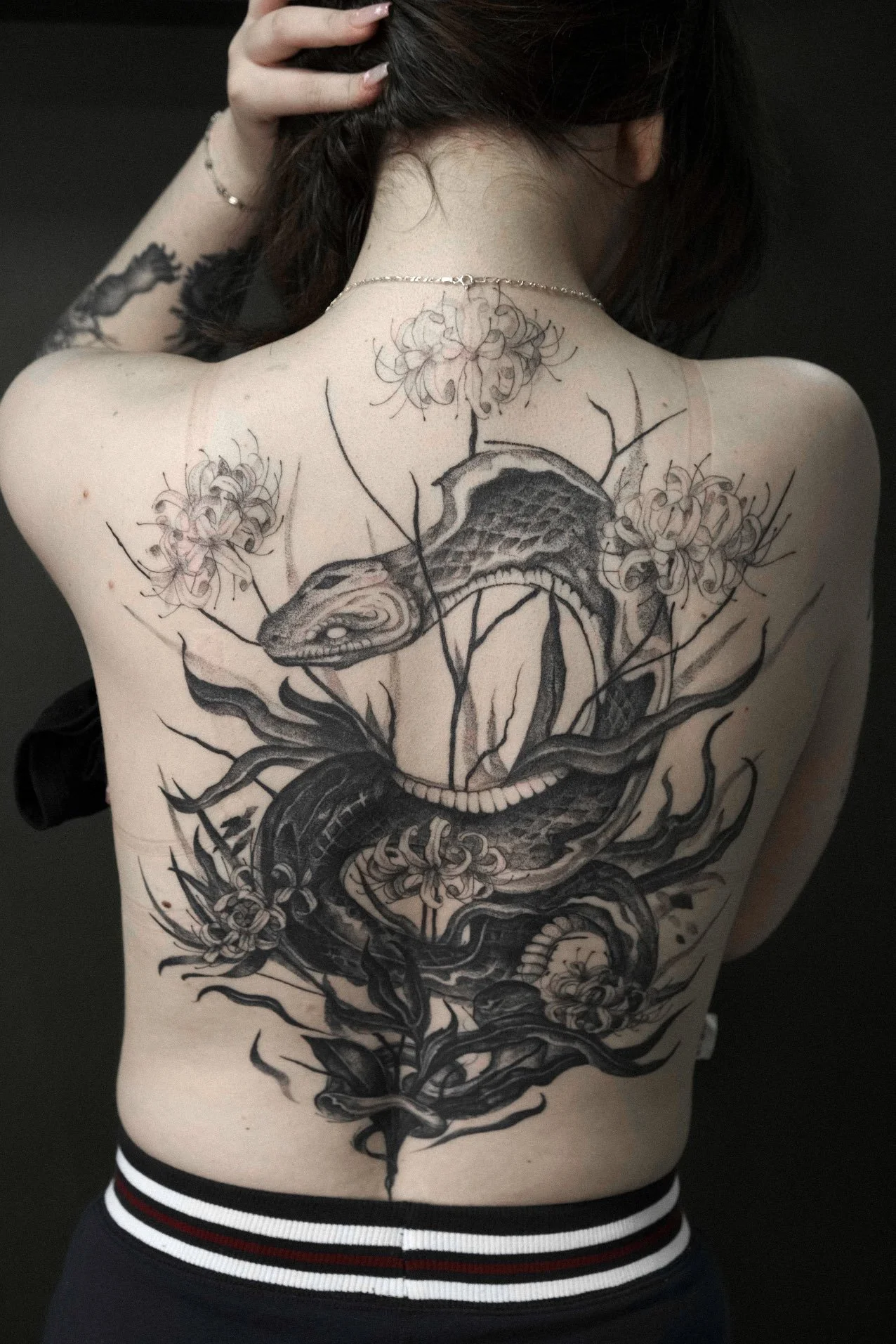 A large, detailed black and gray tattoo of a snake intertwined with flowers tattooed by Jak