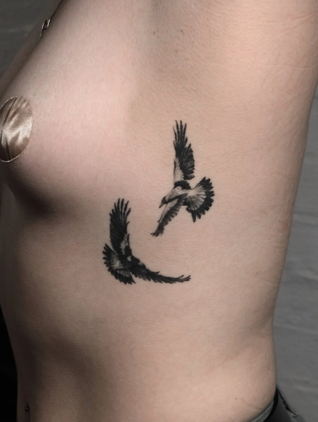 Two micro realism magpies in flight on person's side ribcage tattooed by Jak