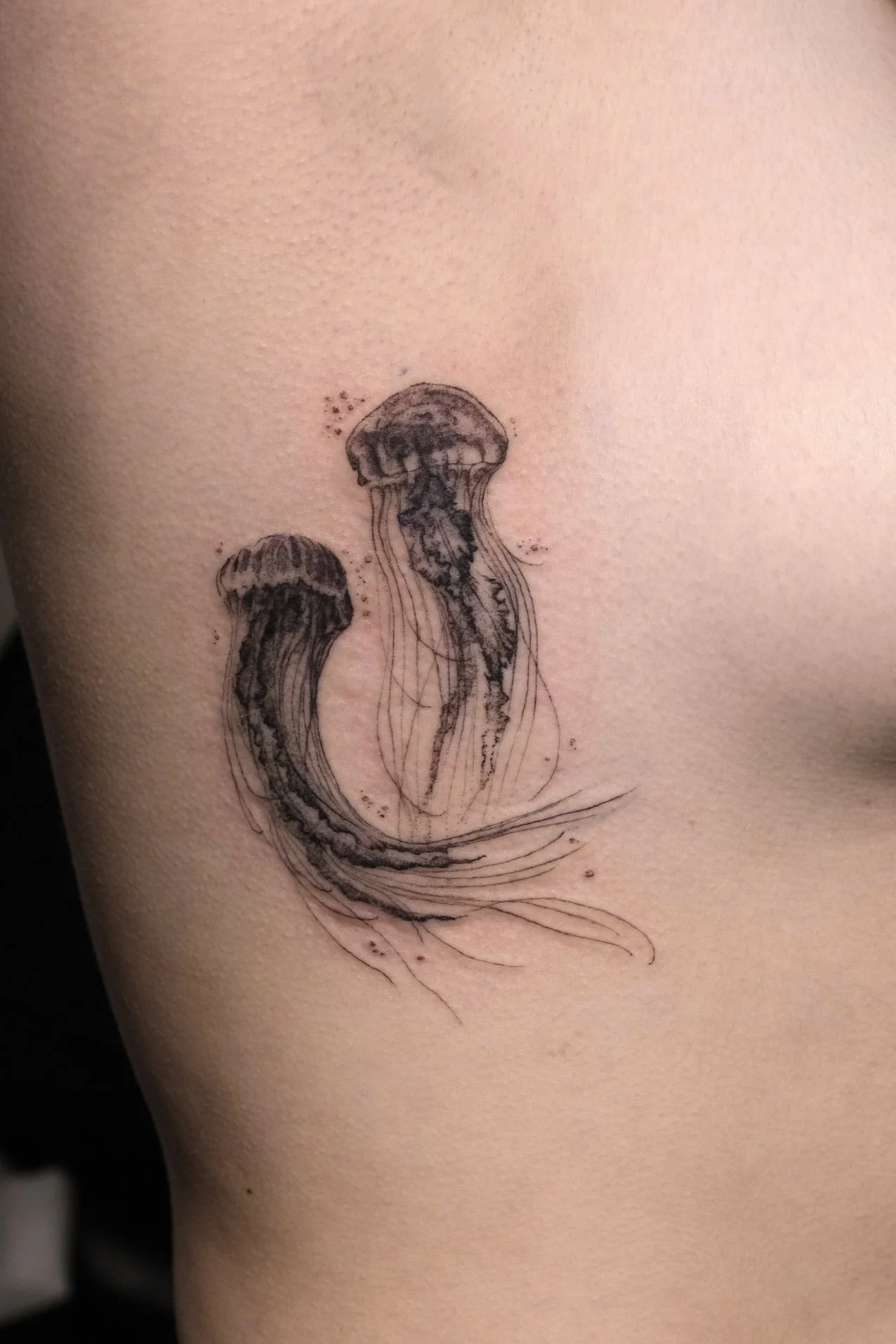 Micro-realism tattoo of two jellyfish on person's ribs by Jak