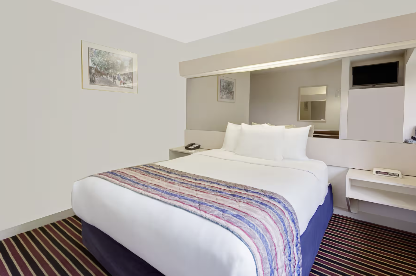 A hotel room with a bed, pillows, nightstands, and a wall mirror.