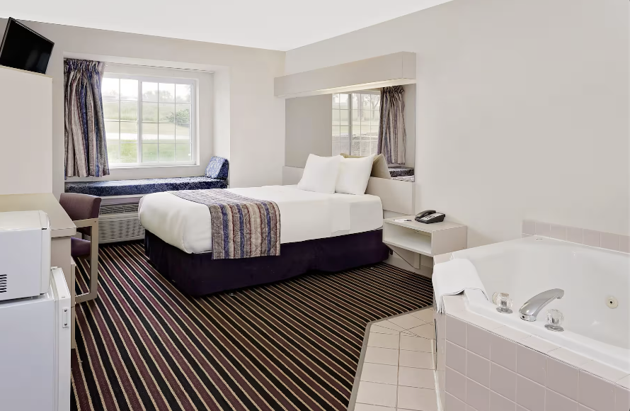 Hotel room with a bed, window seat, and a hot tub.