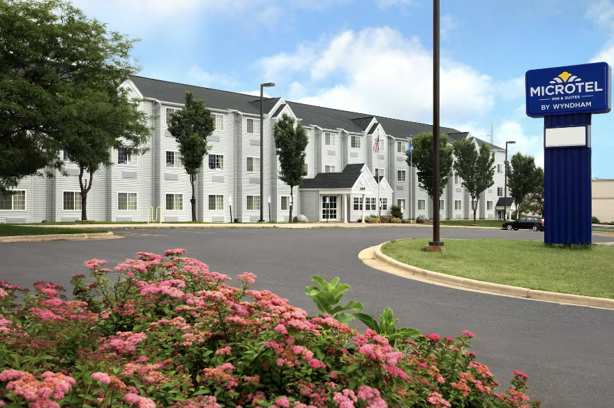 Exterior of a Microtel Inn & Suites hotel with a parking lot, landscaping, and a blue sign