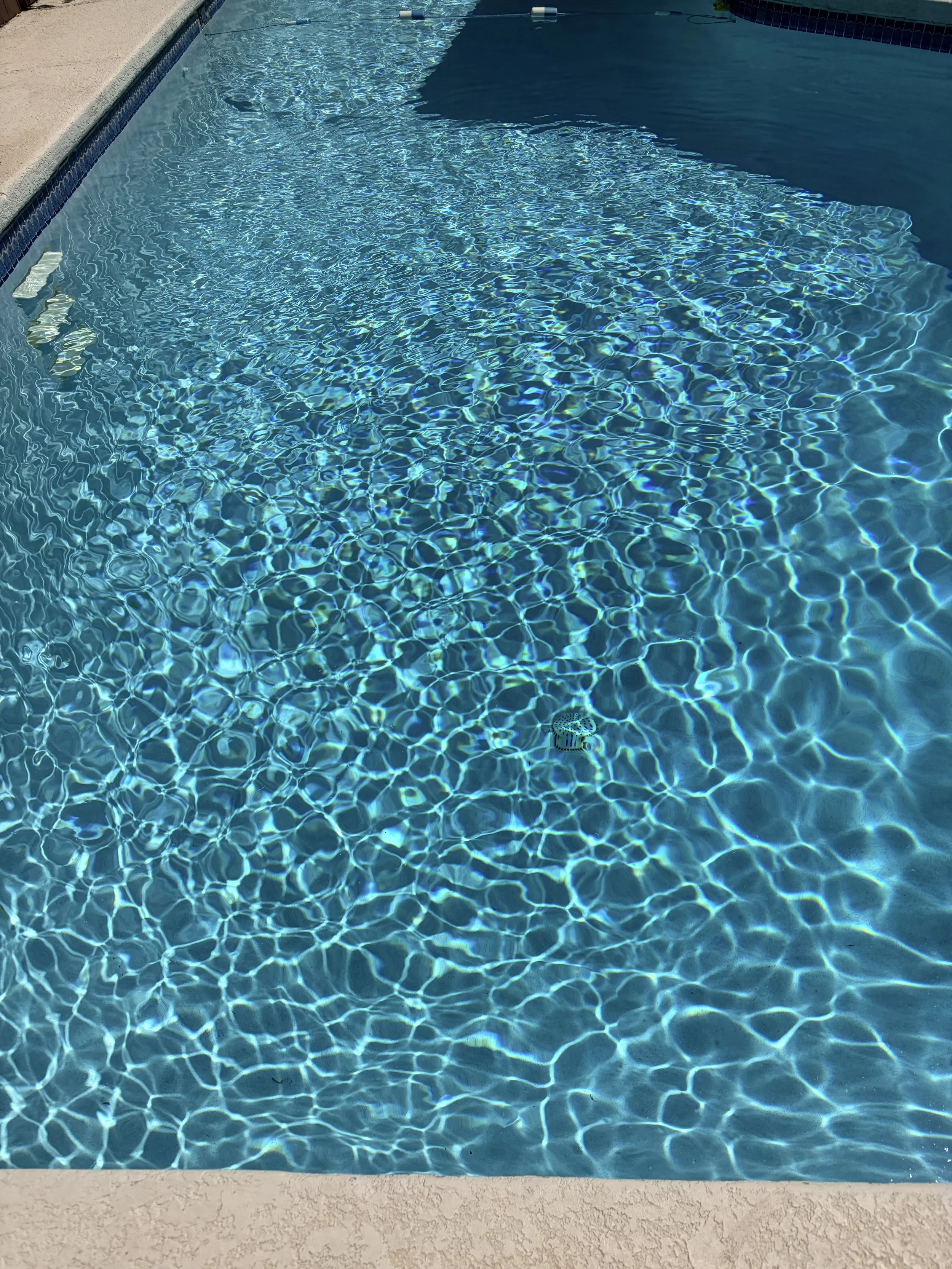 A swimming pool with crystal clear water, blue tile lining, and a textured concrete deck surrounding it.