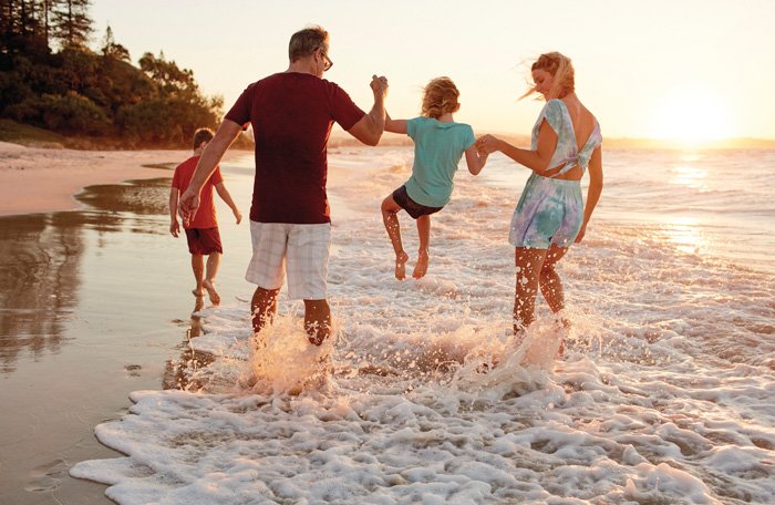 A family of four playing and splashing in the ocean waves during sunset at the beach.