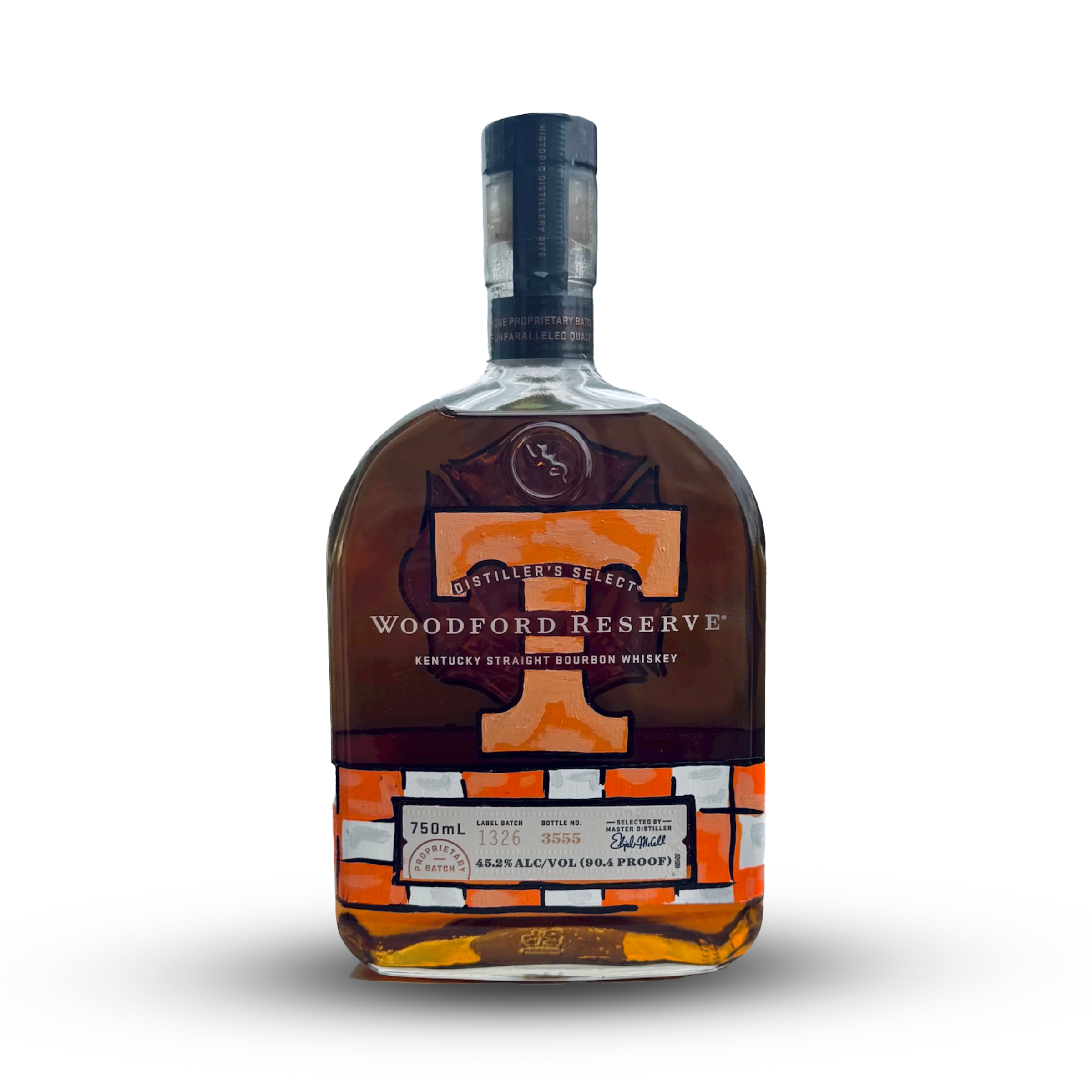 A bottle of Woodford Reserve Kentucky Straight Bourbon Whiskey with a black and orange label, and clear glass showing the amber-colored liquid inside. Custom artist liquor label that has University of Tennessee Knoxville.