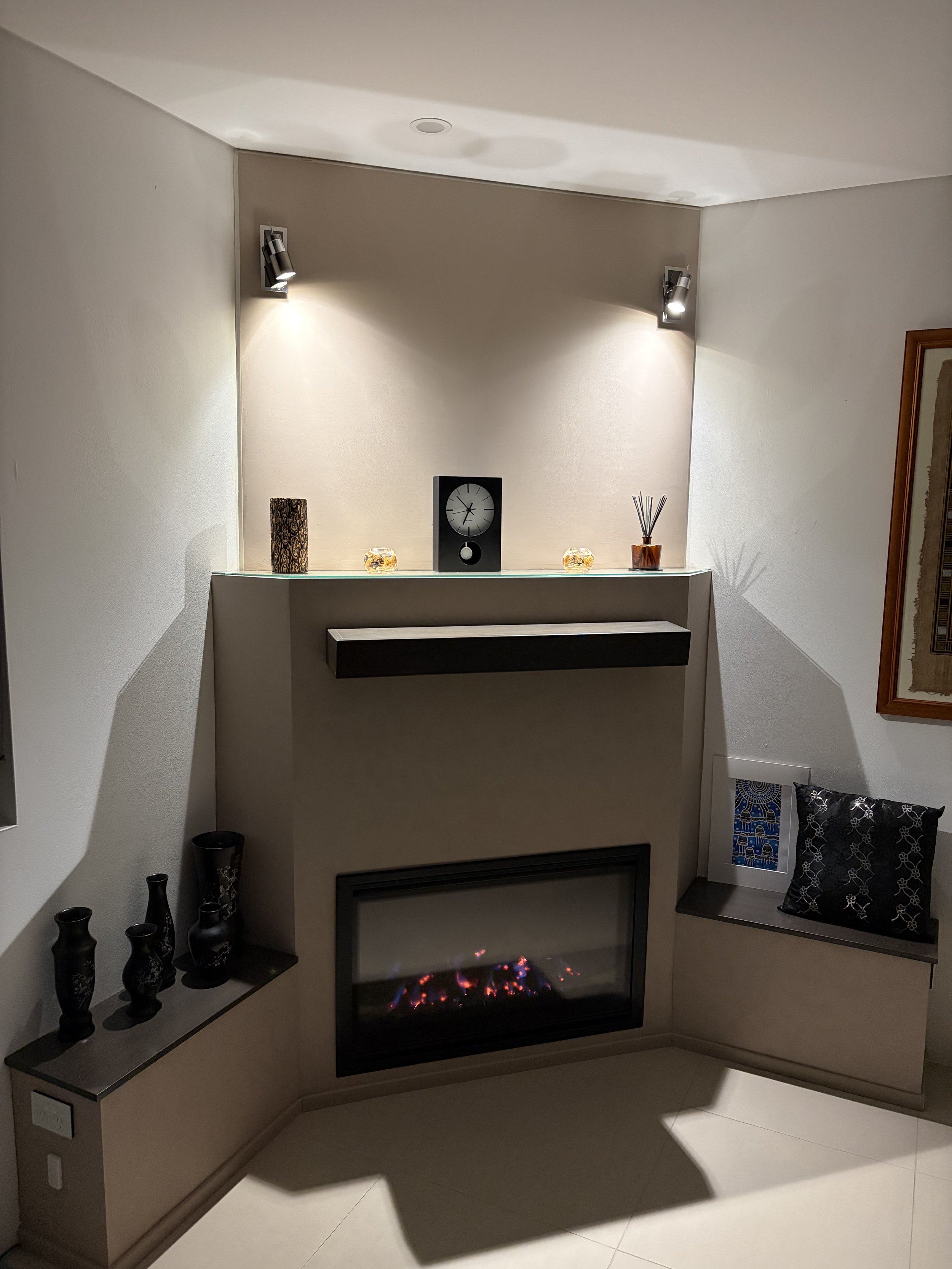 Living room corner with fireplace, decorative vases on side table, clock, reed diffuser, and framed artwork on wall.