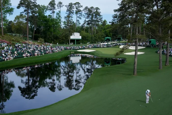A golfer preparing to putt on a golf course surrounded by water and spectators watching from the sidelines.