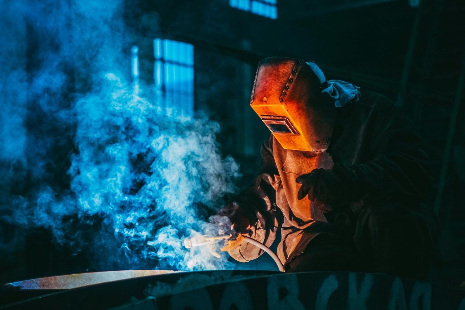 man in protective clothing using a welding torch creating welding fumes