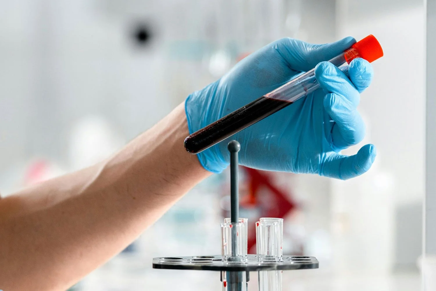 close up of gloved hand holding vial of blood during environmental exposure monitoring