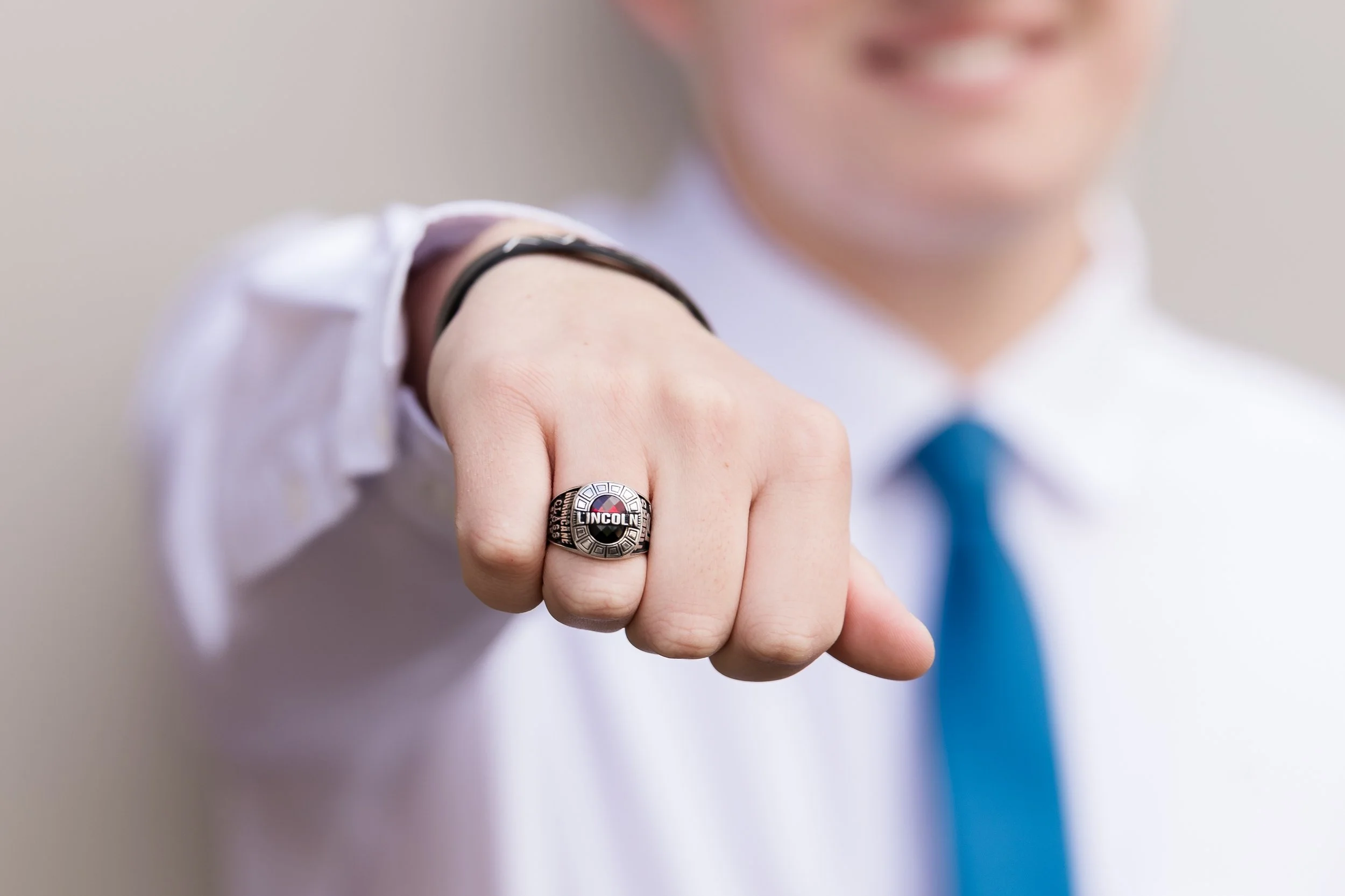 a senior boy dressed in a white shirt and tie out of focus with his knuckles showing off his class ring in focus