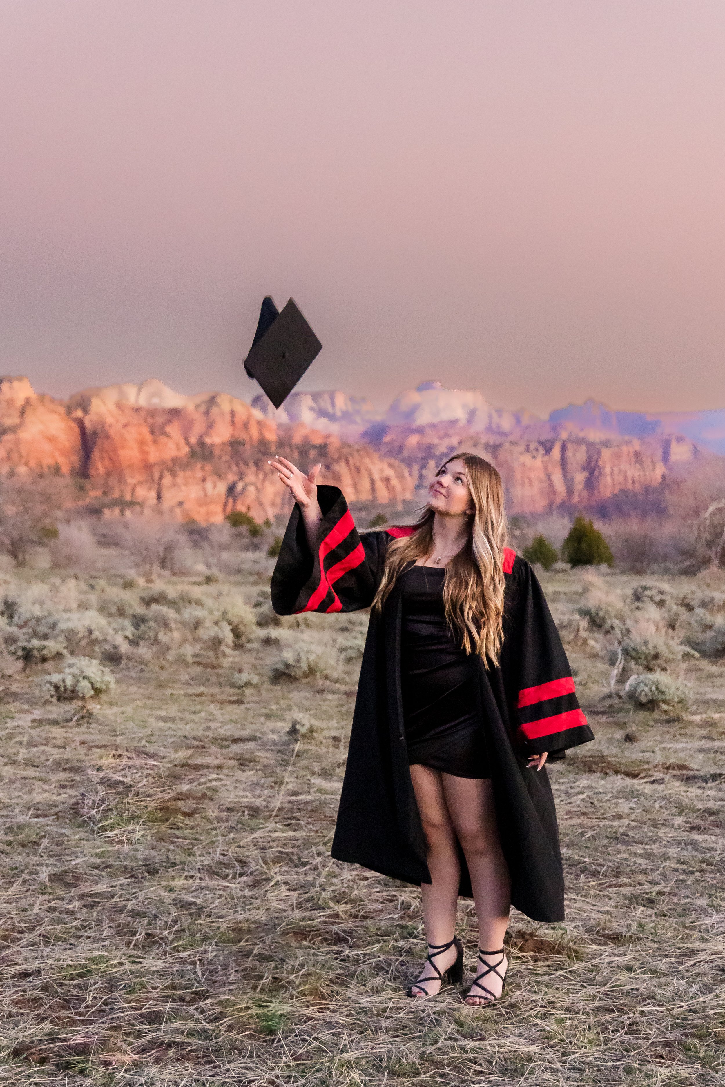 senior girl wearing a graduation gown and tossing her cap into the air with zion in the background