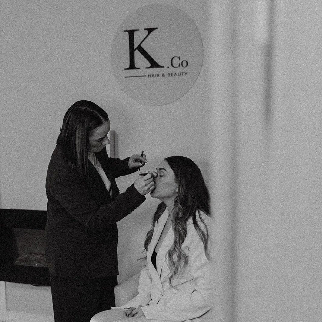 A woman getting her makeup applied by another woman in a hair and beauty salon.