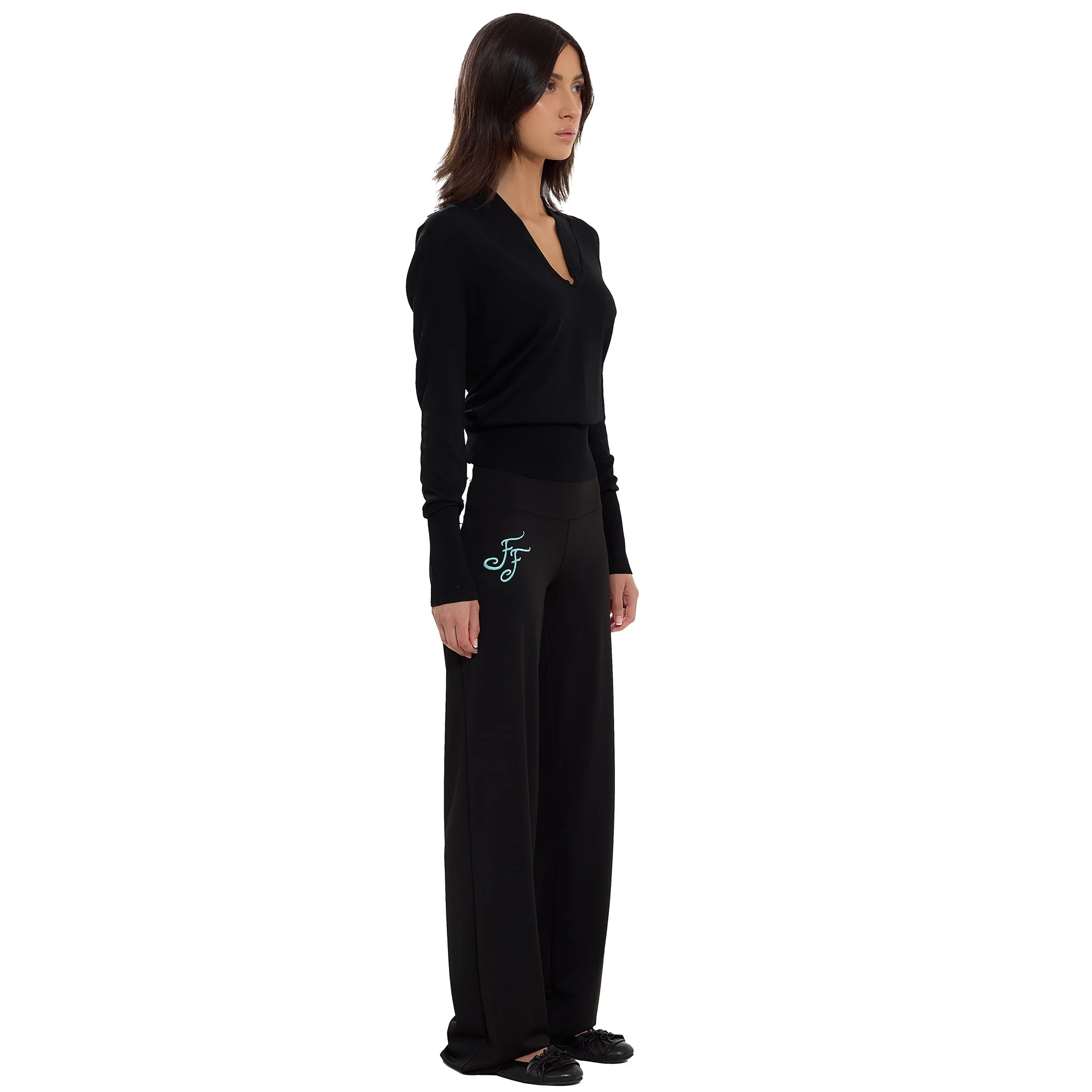 A woman with medium-length brown hair wearing a black long-sleeve shirt and black pants standing against a white background.