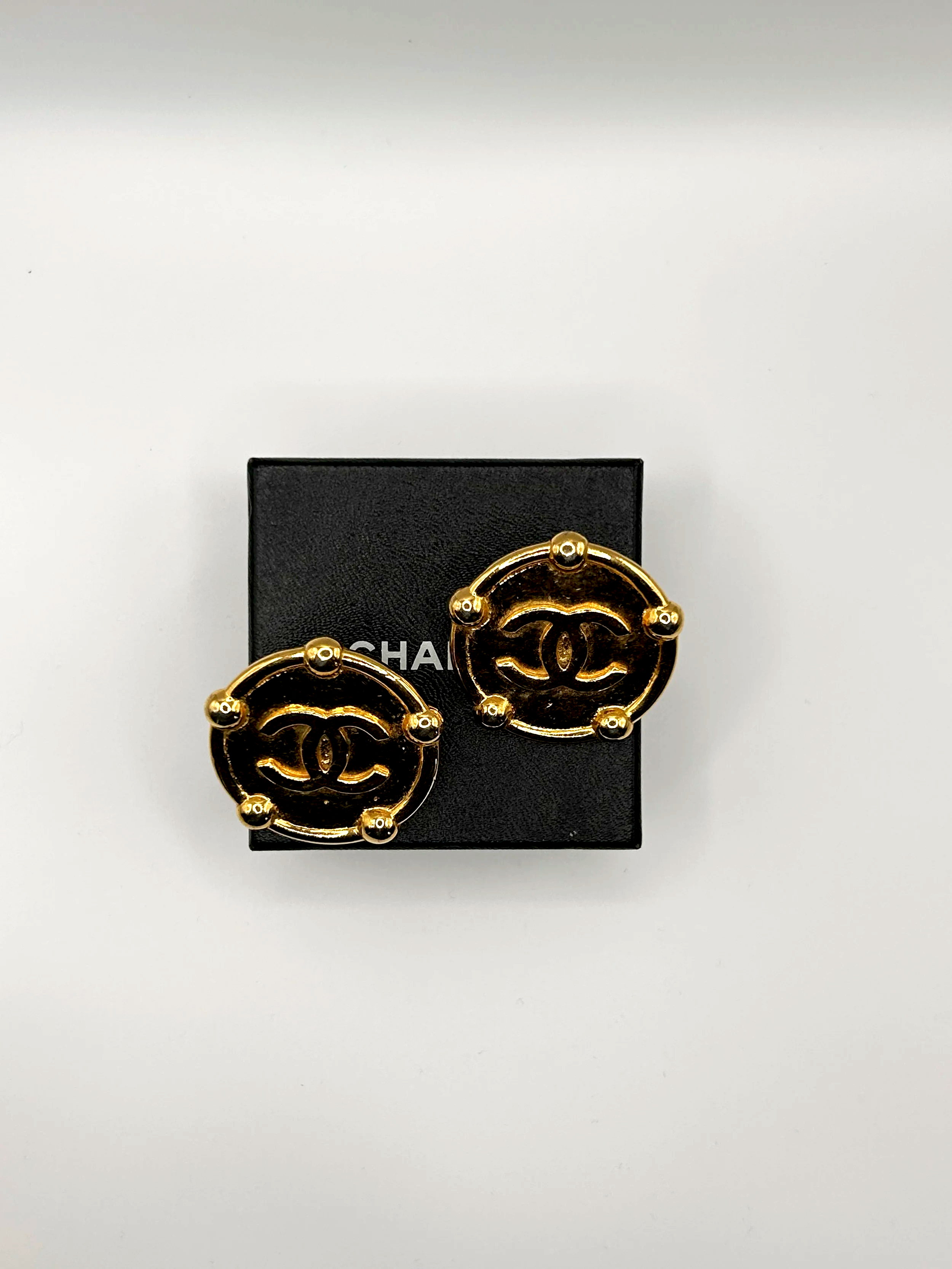 Gold Chanel earrings with interlocking 'CC' logo on a black box with white background.