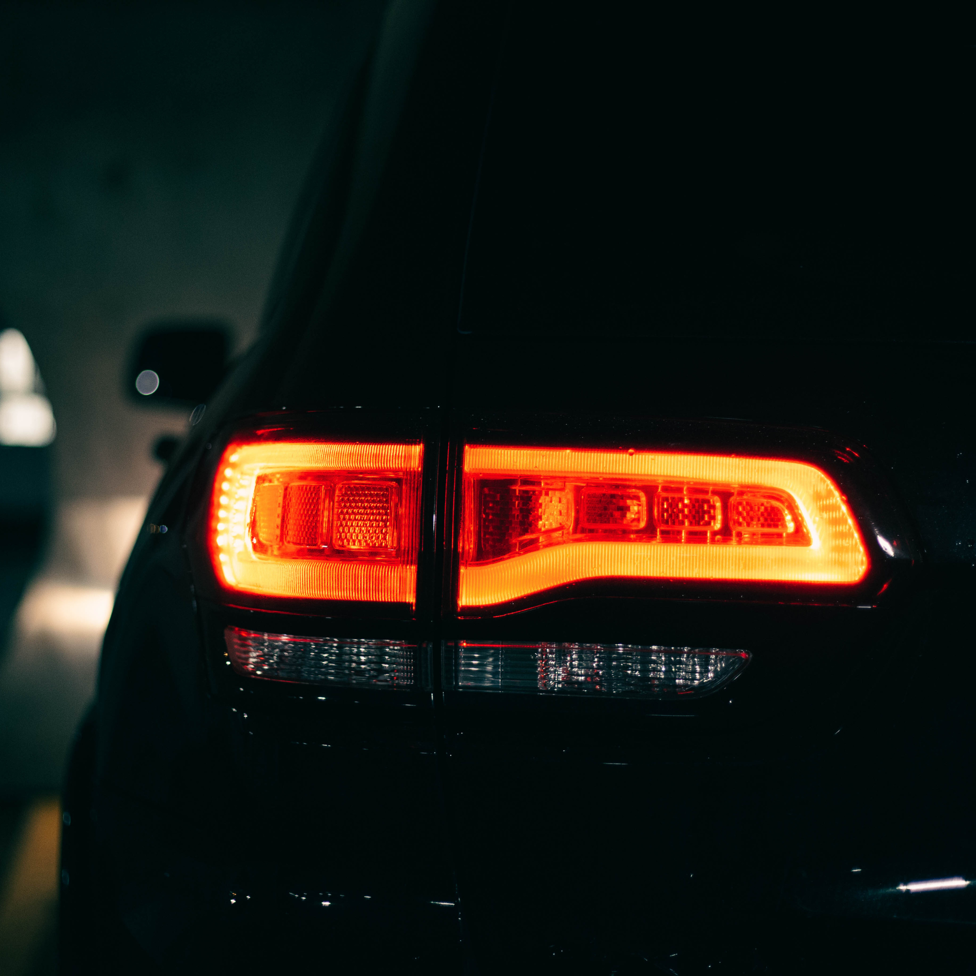 The rear of a black car with illuminated red taillights, shot in a dark setting.