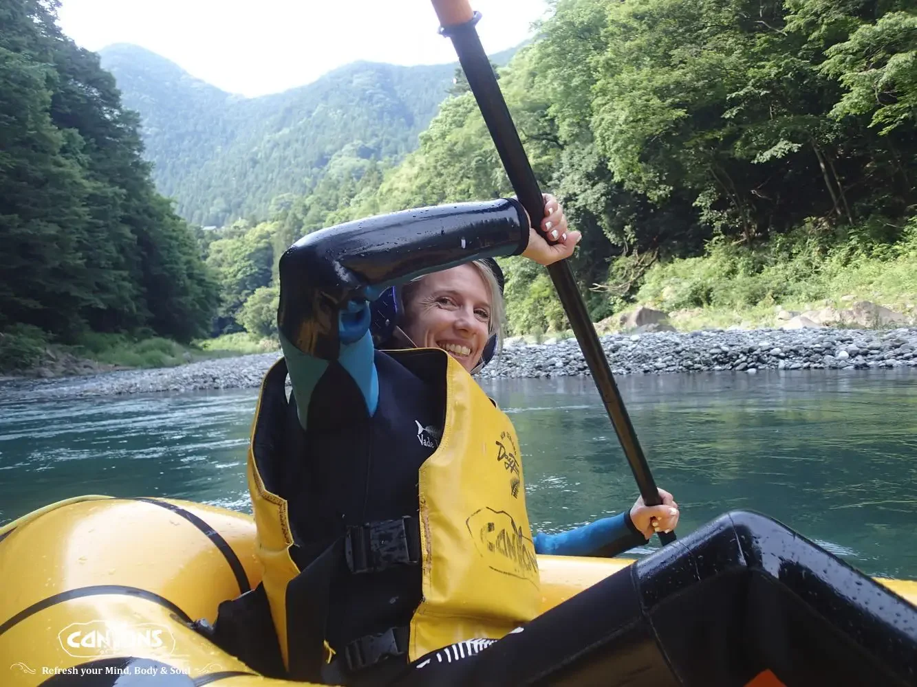 Woman kayaking on a river surrounded by green trees and mountains.