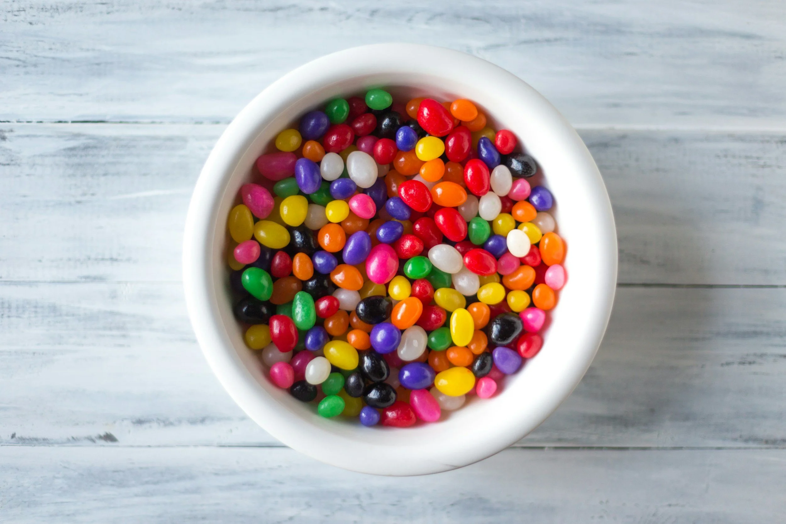 Tazón blanco lleno de gomitas de colores sobre una superficie de madera clara.