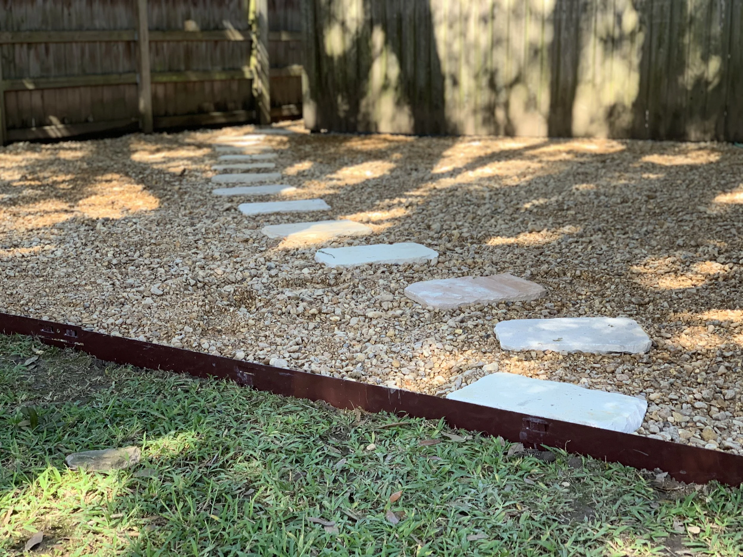 A backyard paver walkway with decorative gravel outlined with brown metal edging installed by J&B Lawn & Landscaping.
