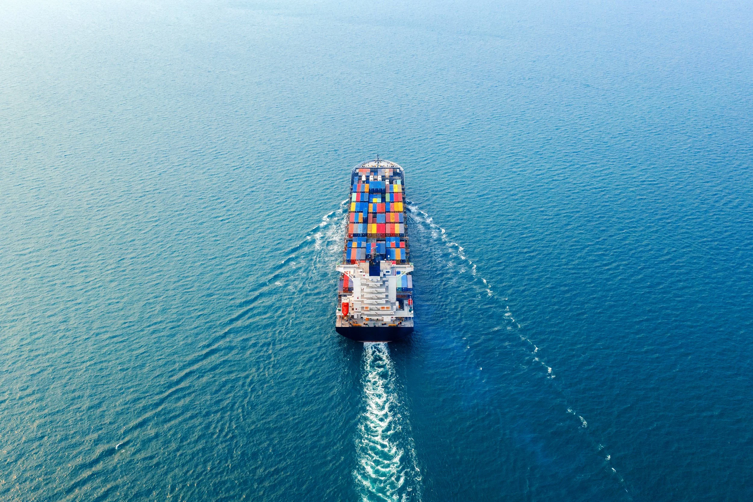 A cargo ship with colorful containers sailing through the ocean, viewed from above.