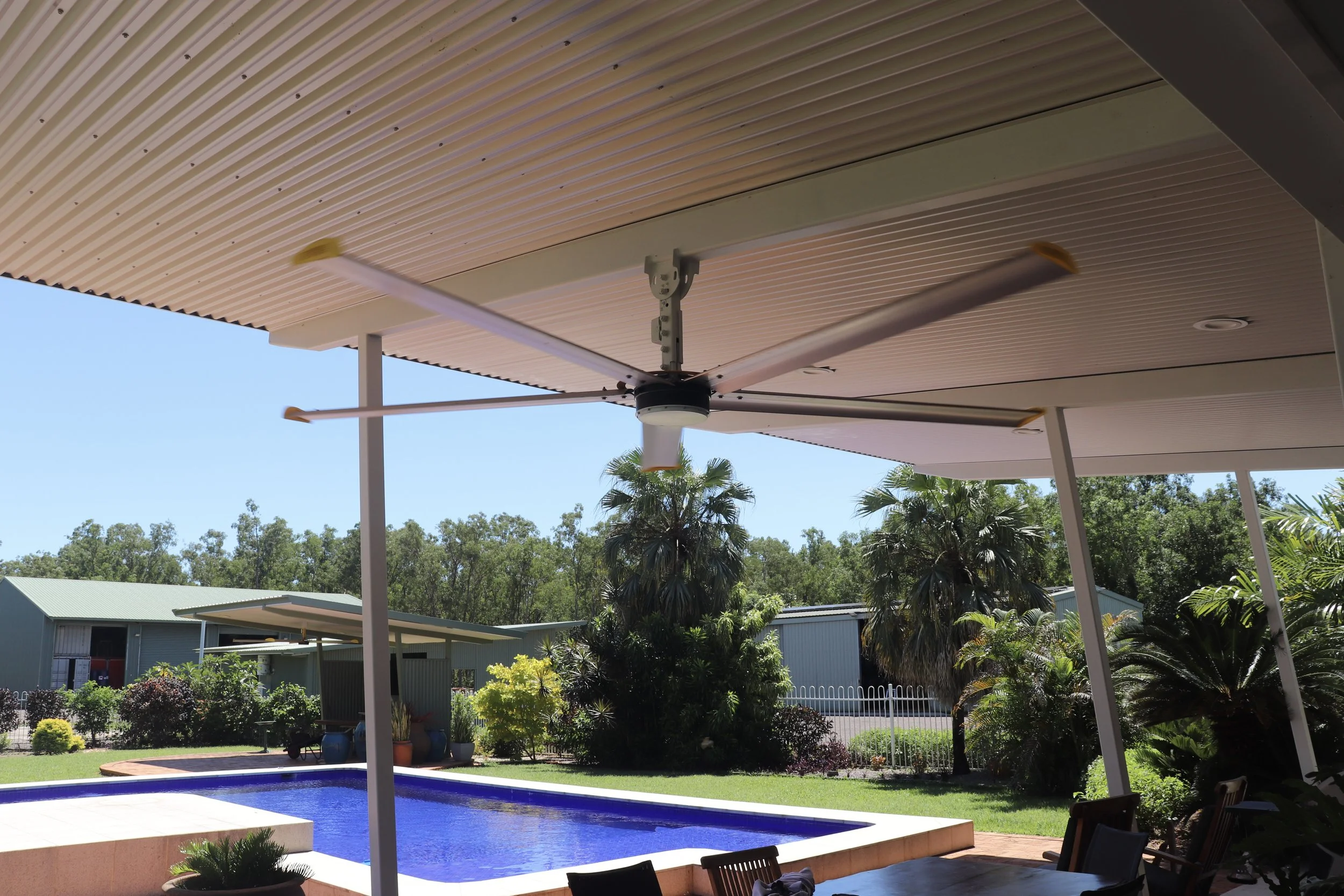 A backyard scene with a swimming pool, patio, and outdoor structures under a clear sky. Residential small HVLS fan Darwin