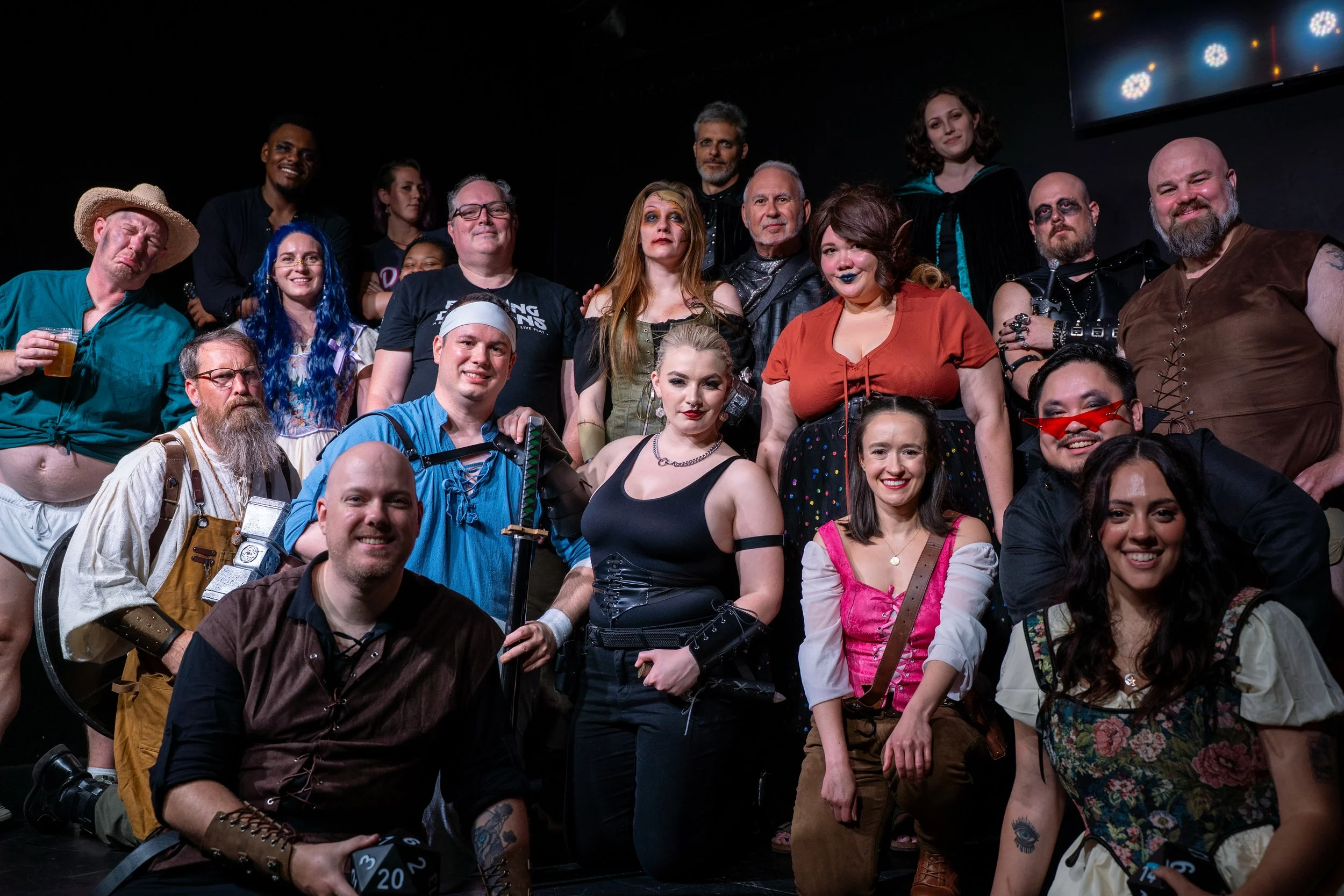 Group of people in costume, dressed as pirates, adventurers, or fantasy characters, posing on a stage with a dark background and some stage lights.