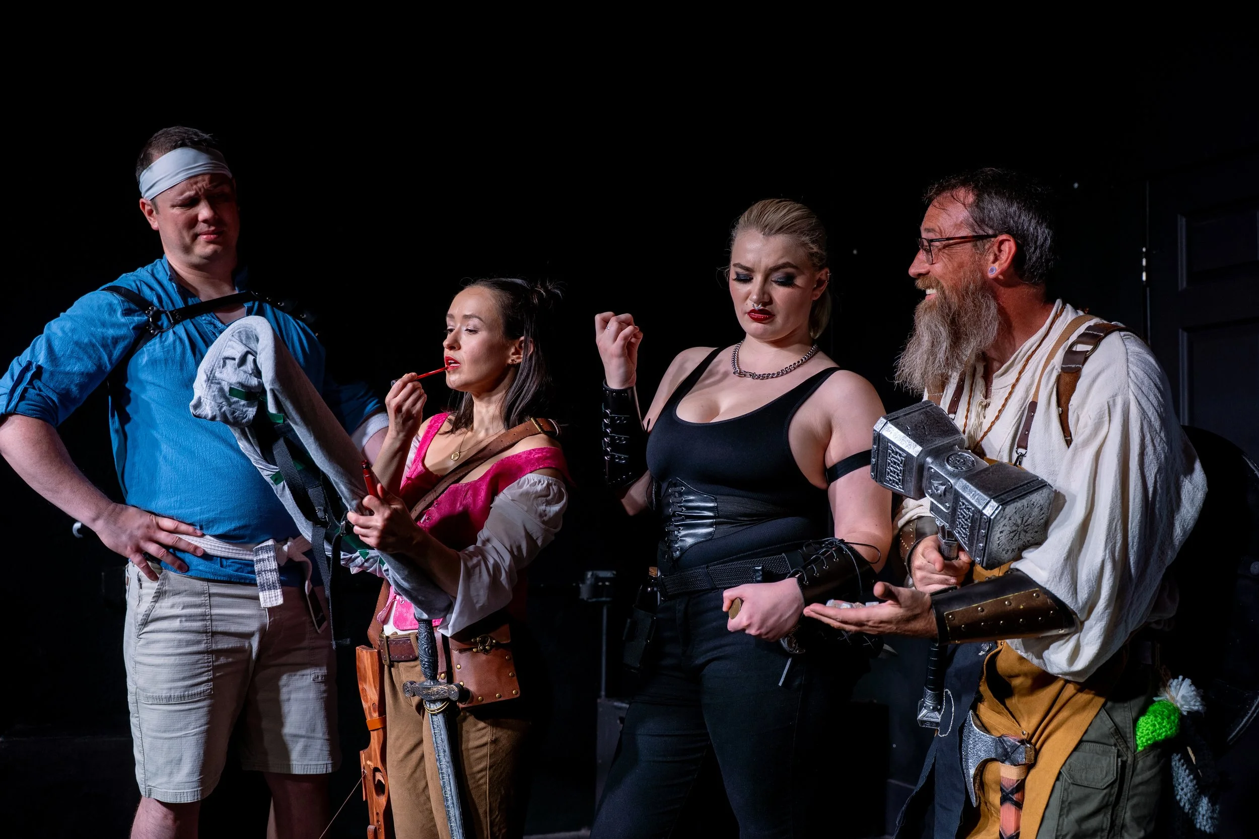 Four actors on stage in costume, with black background and theatrical lighting.