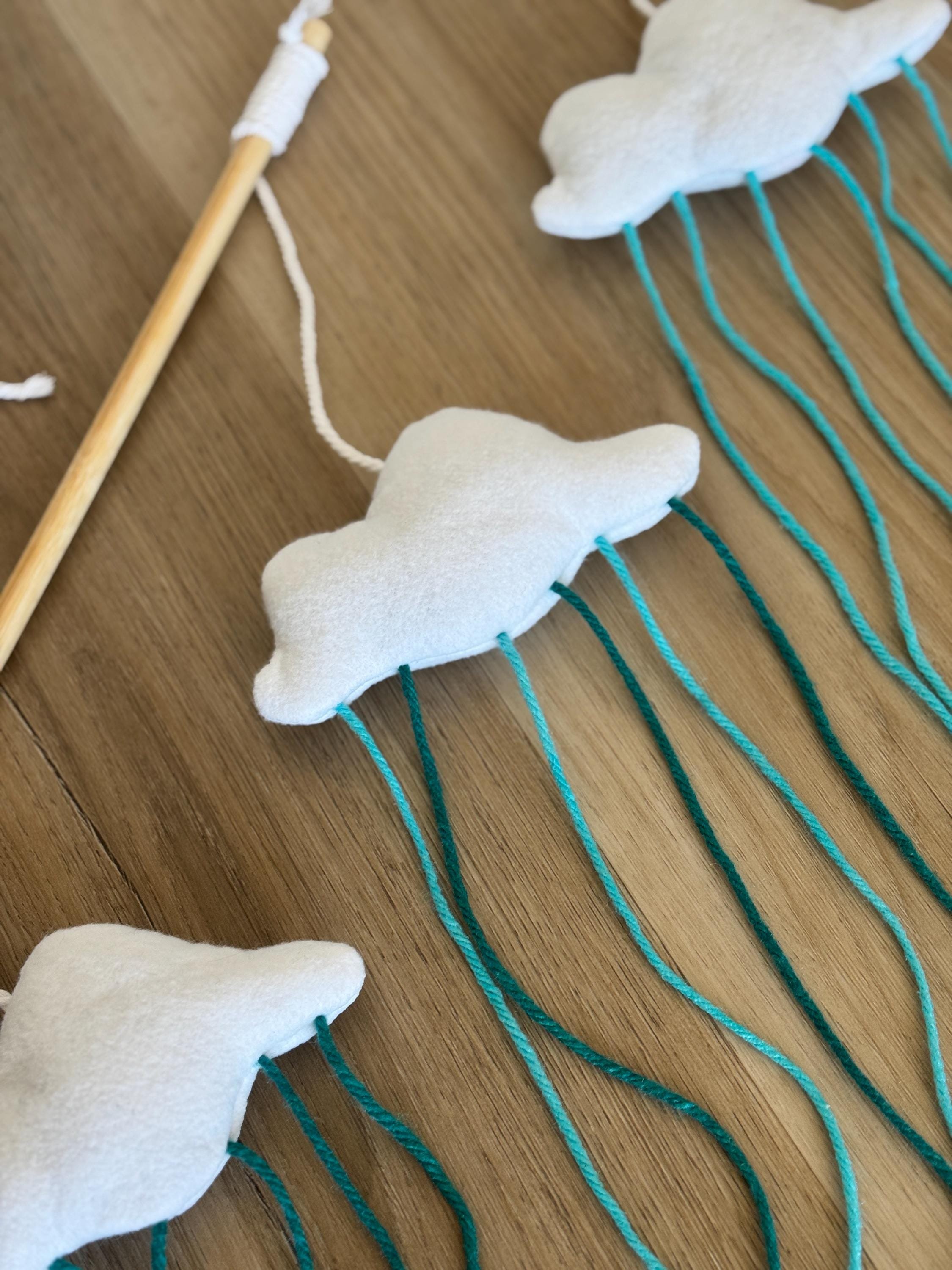 Close-up of stuffed cloud cat wand toys with hanging teal strings. Displayed on a wooden floor surface.