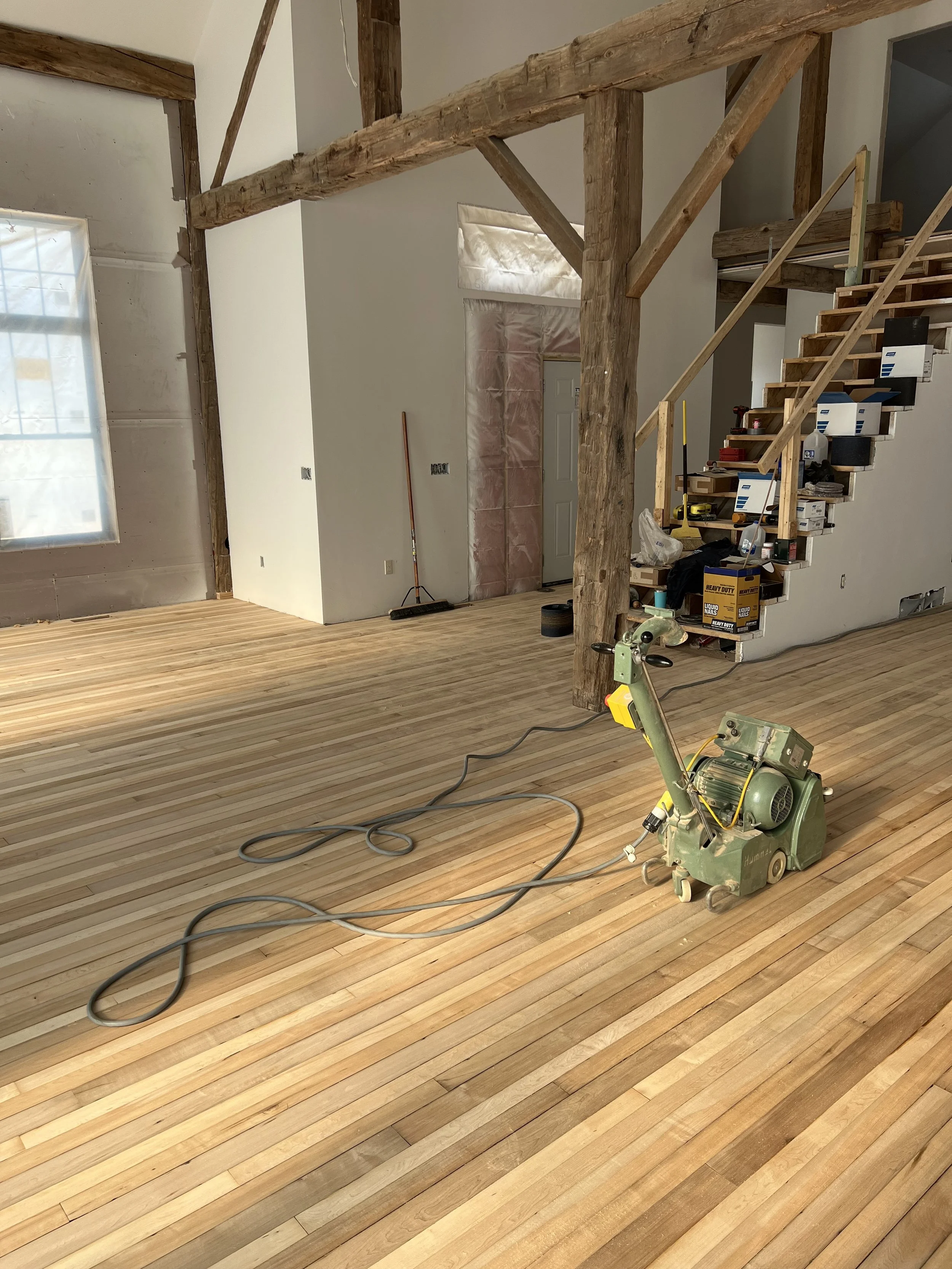 Interior view of a room under construction with a wooden staircase, construction tools, and a wood floor.