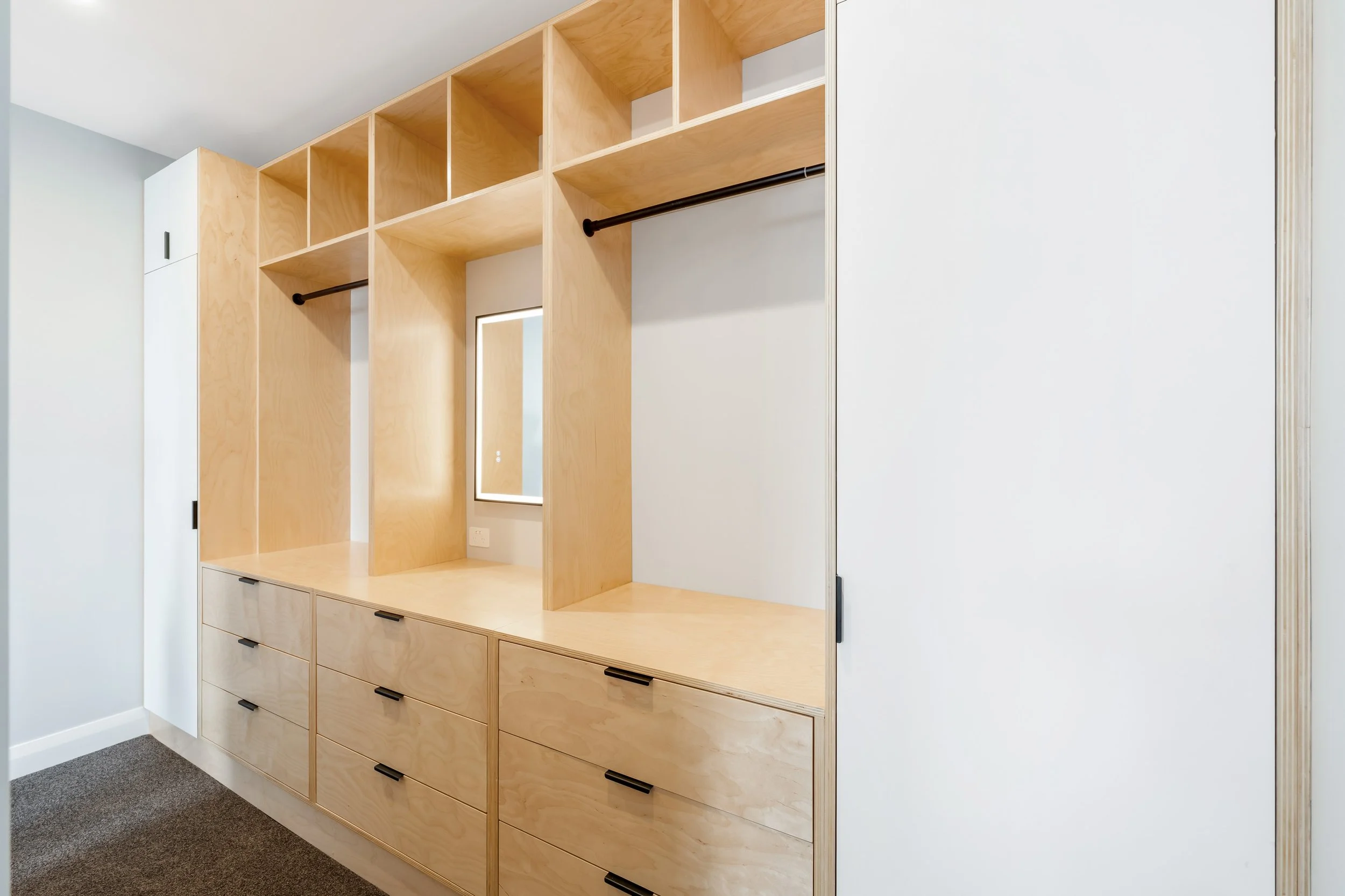 Empty built-in closet with wooden shelving, drawers, and black handles, including a mirror and a small window.