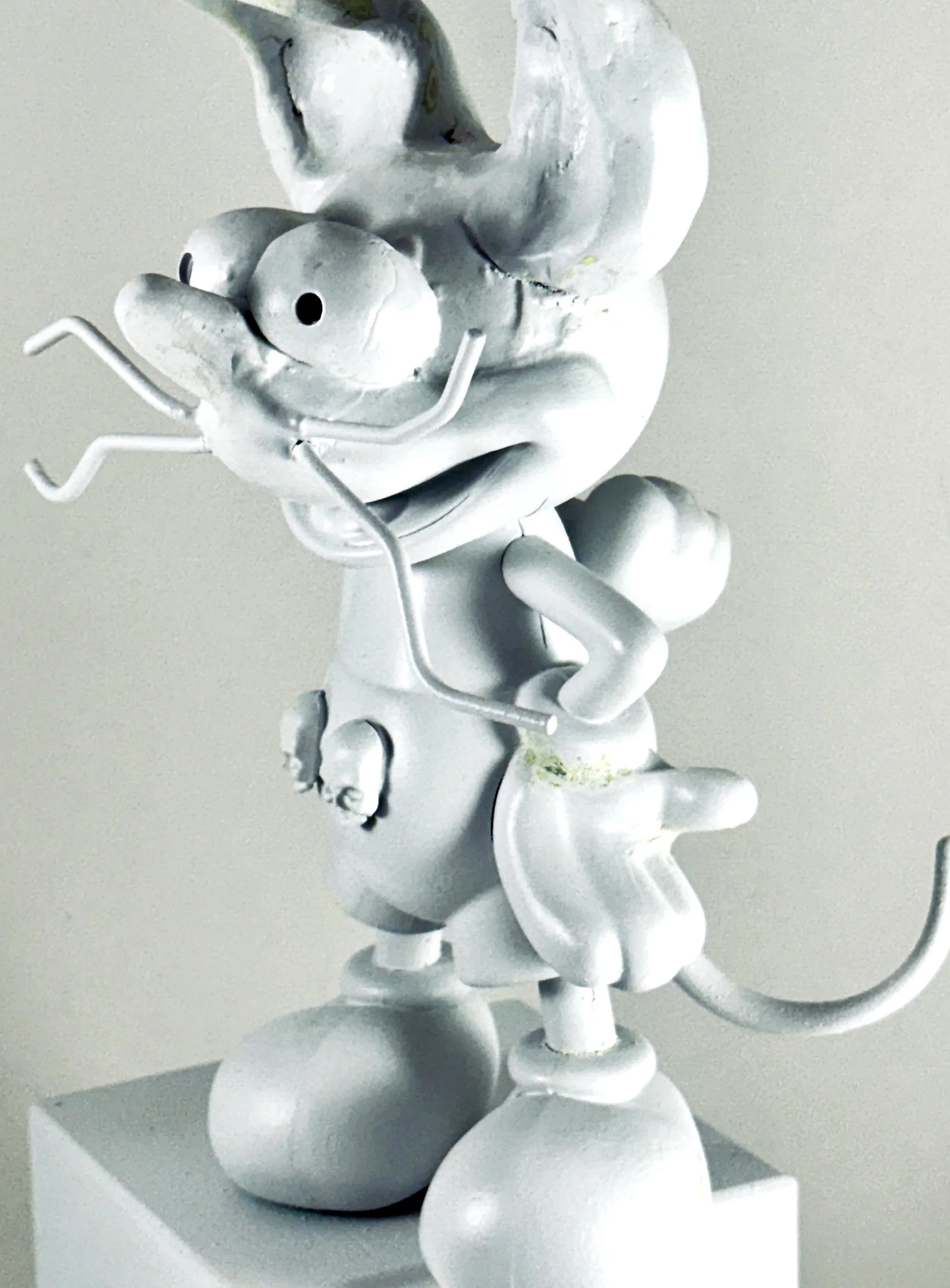 A sculpture of a dog with a small snake in its grasp, made of metallic material with a shiny, reflective surface, placed on a white pedestal.