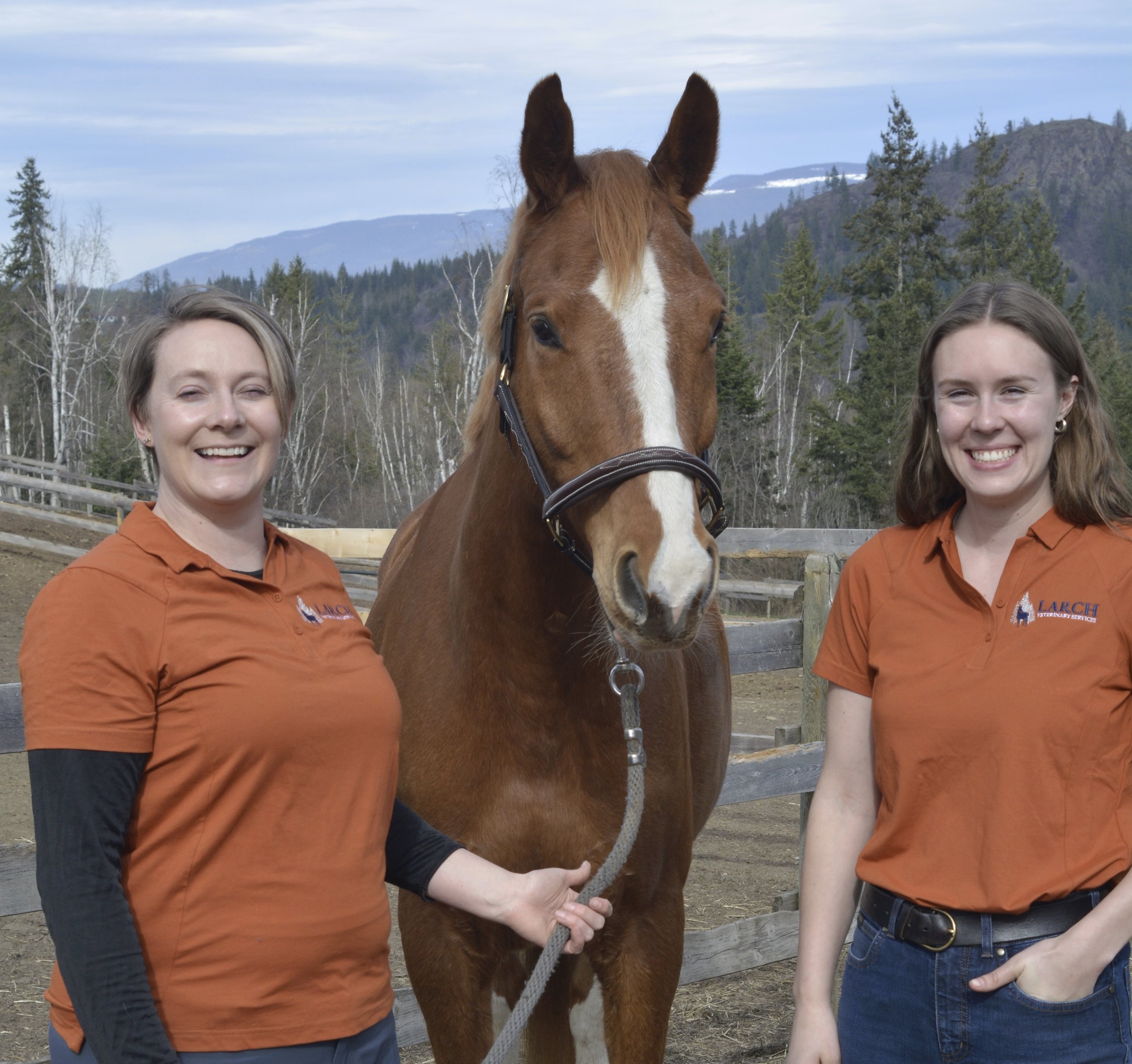 Two women and a horse outdoors with mountains and trees in the background.