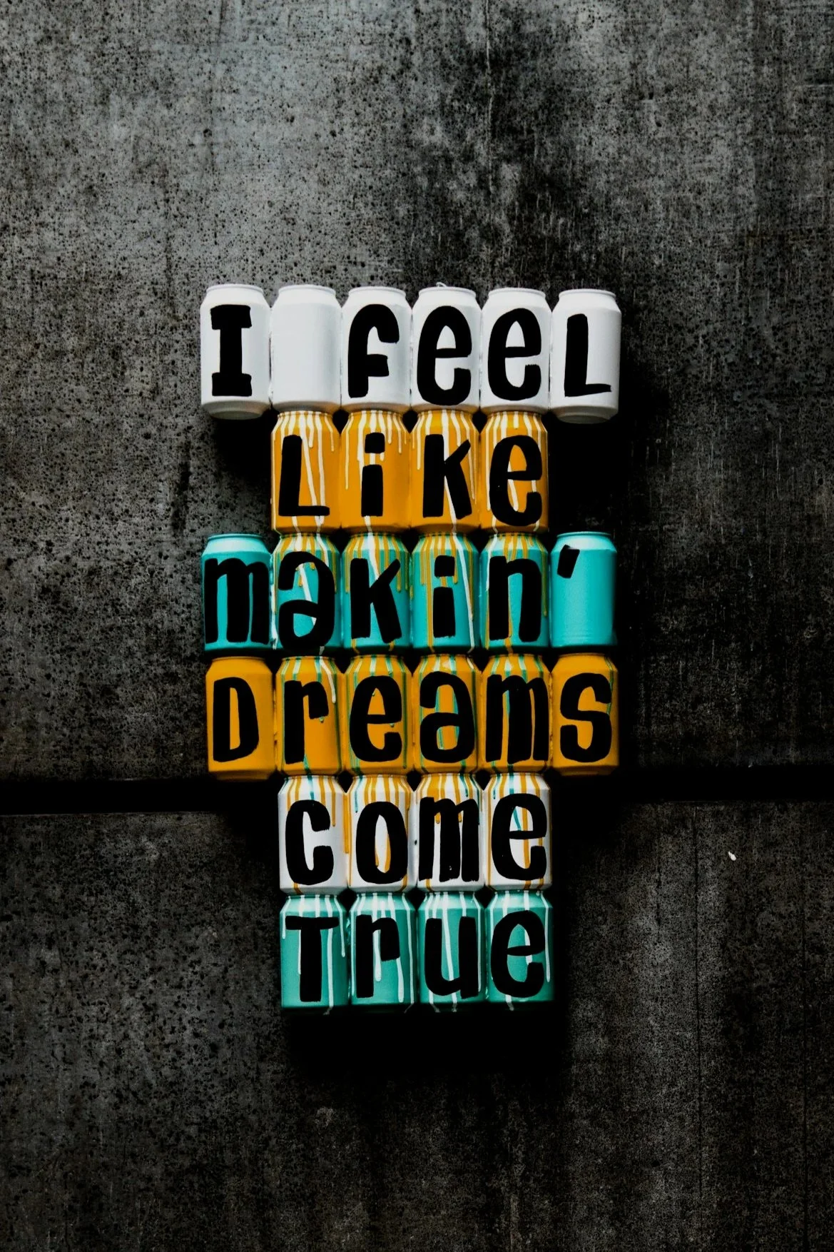Colorful cans arranged to spell out the phrase: "I feel like making dreams come true" on a dark textured background.