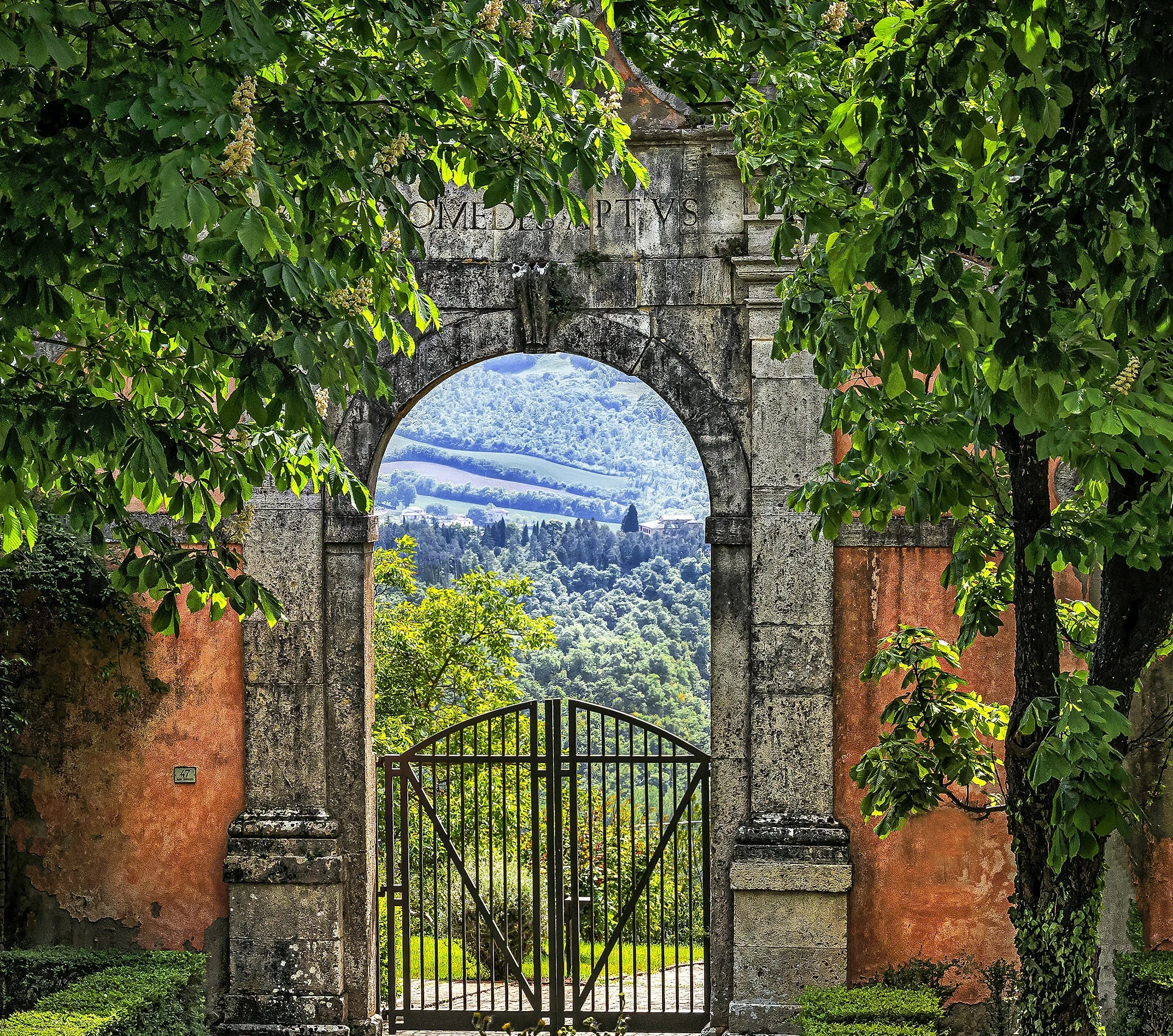 Wrought iron gate and ivy-covered stone archway opening to rolling vineyards in Tuscany, Italy, a curated itinerary by Willow & Wander Travel.
