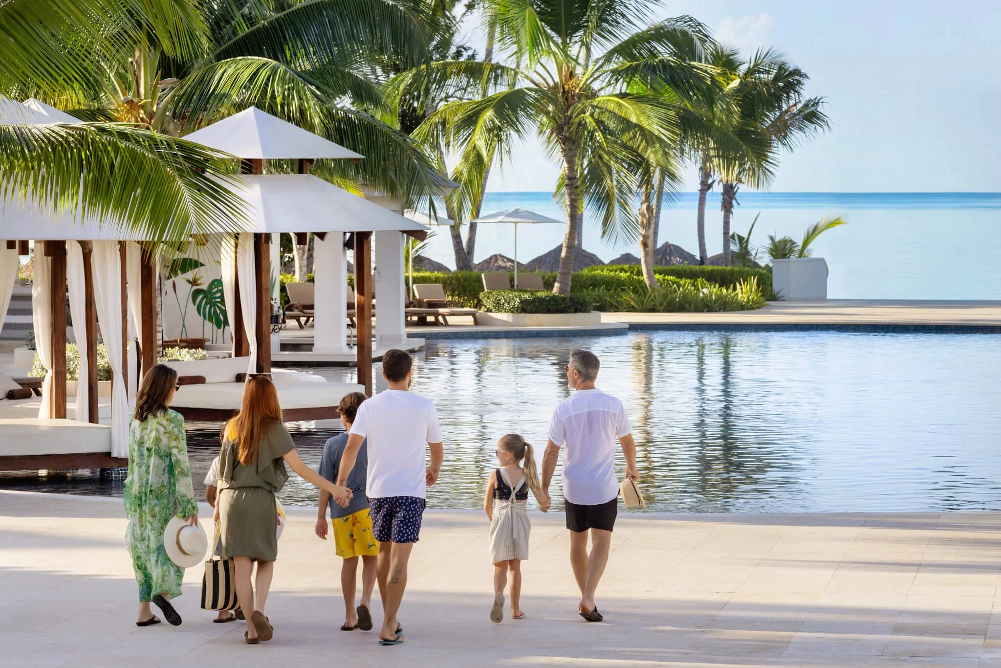 A multi-generational family walking through a luxury all-inclusive pool area at sunset; an intentional family discovery curated by Willow & Wander Travel.