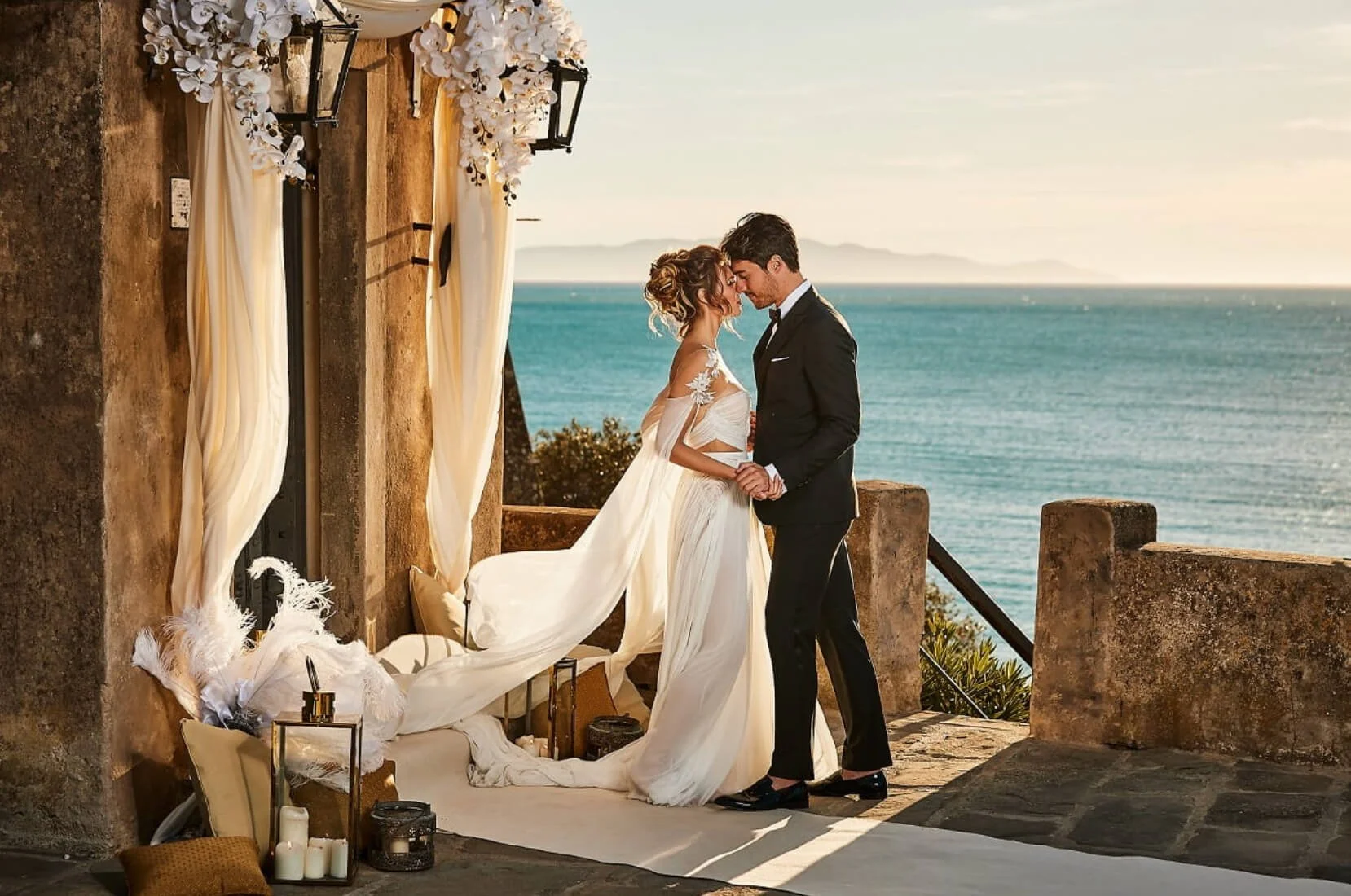 A bride and groom on a clifftop balcony at the historic Torre di Talamonaccio in Tuscany; a signature romantic discovery curated by Willow & Wander Travel.